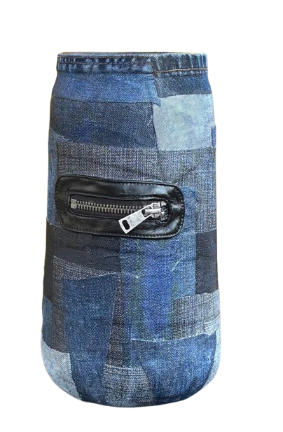 Een blauwe, patchwork denim drankkoeler met een klein zwart leren ritsvakje, afgebeeld tegen een wazige gele achtergrond.