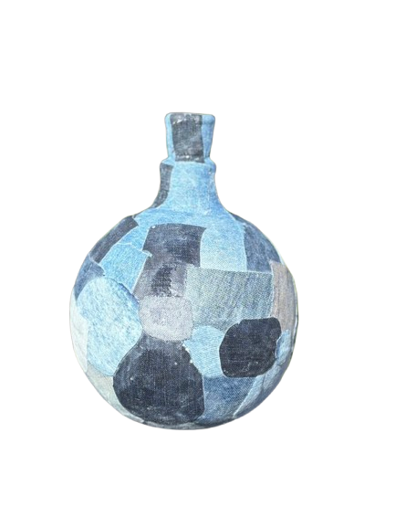 Een glazen fles met blauw mozaïekpatroon op een donker doek, met een wazige achtergrond van bladeren.