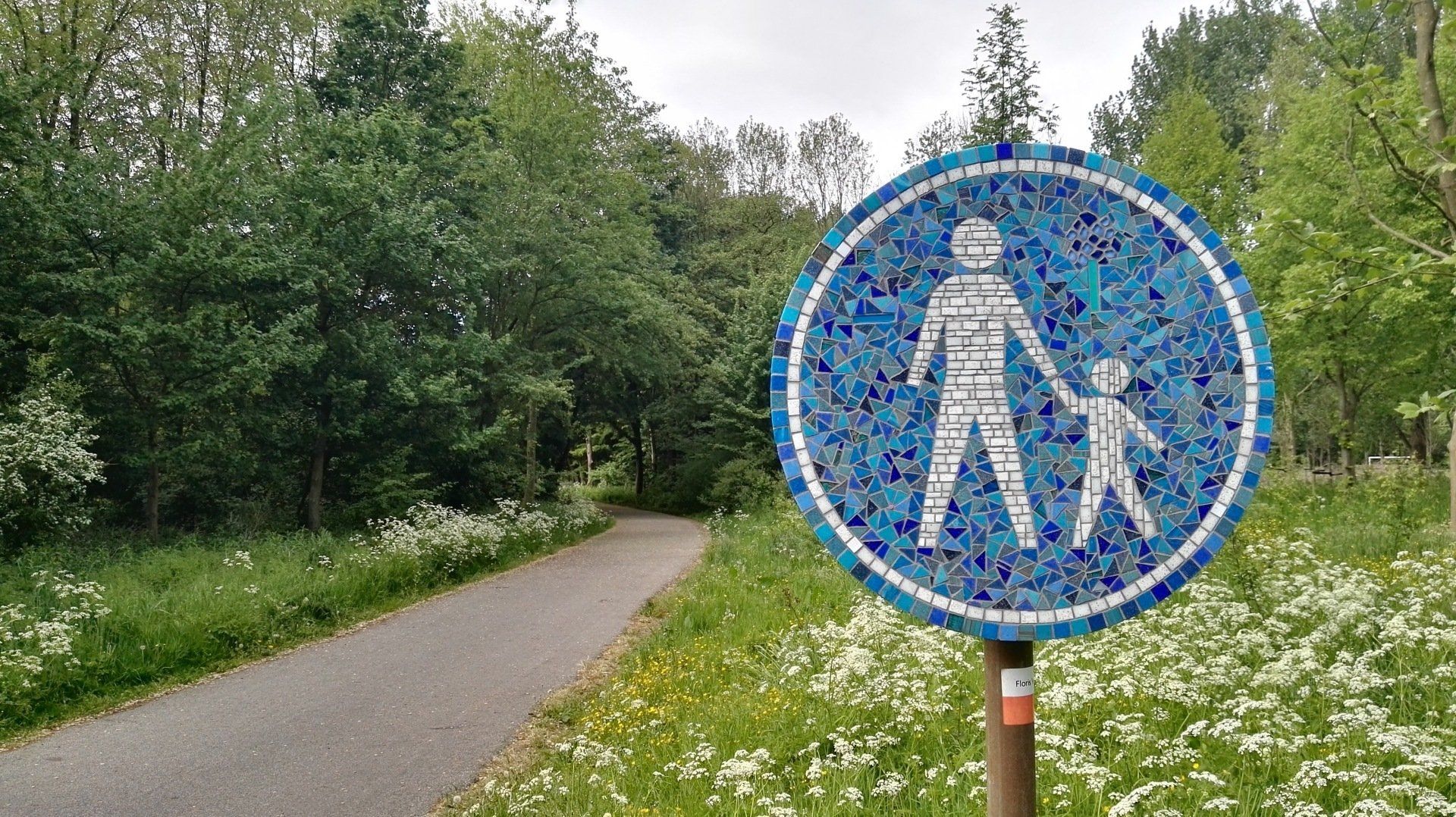 Een blauw-wit mozaïek verkeersbord met daarop een persoon en een kind