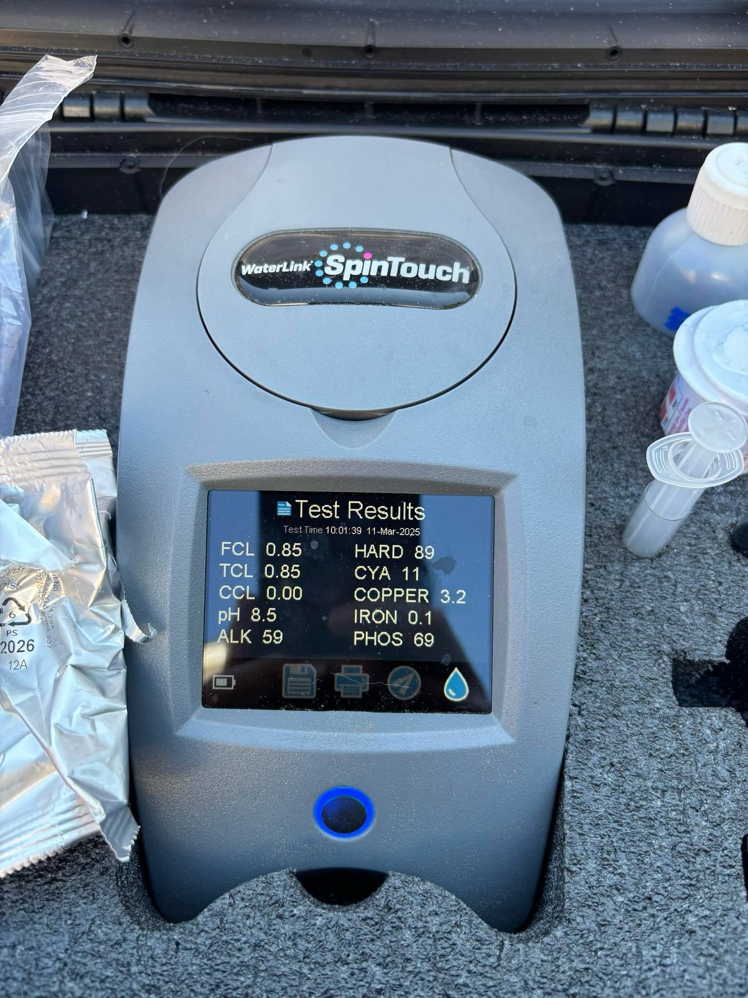 Two men in gloves drain a pool with a hose, near bushes on a sunny day.