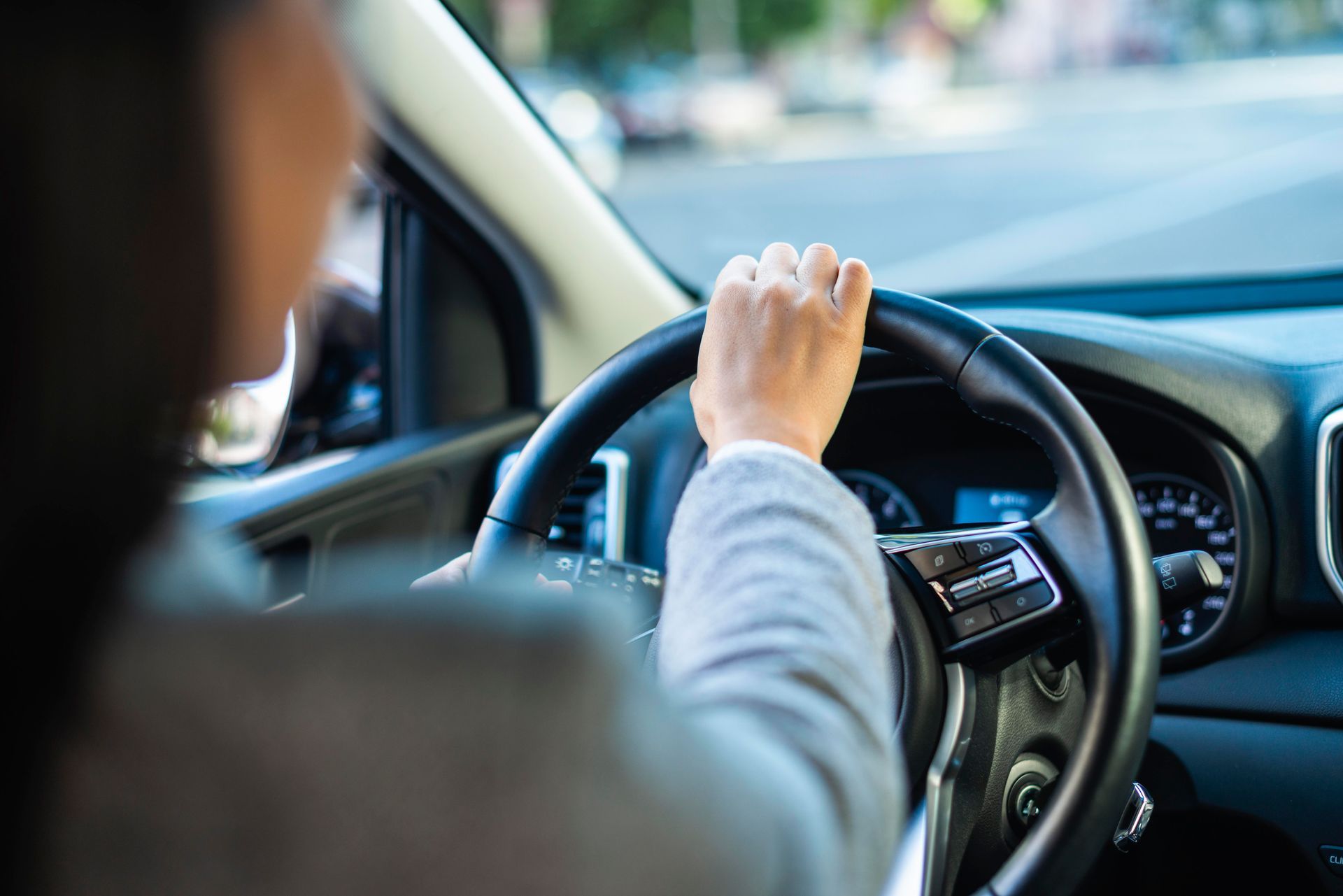 A woman is driving a car with her hand on the steering wheel.