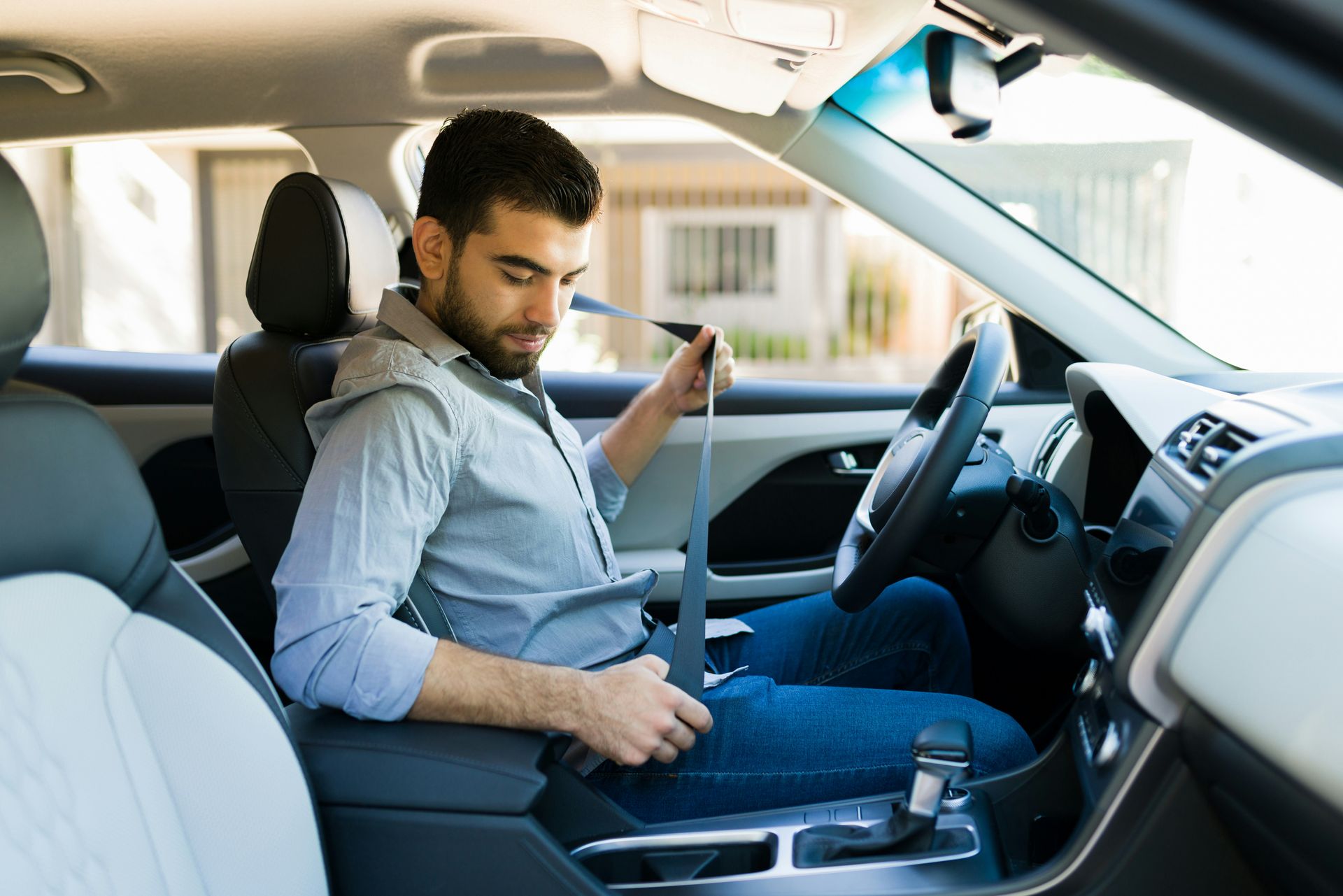 A man is sitting in the driver 's seat of a car adjusting his seat belt.