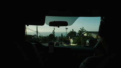 A woman is sitting in the back seat of a car holding a cell phone.