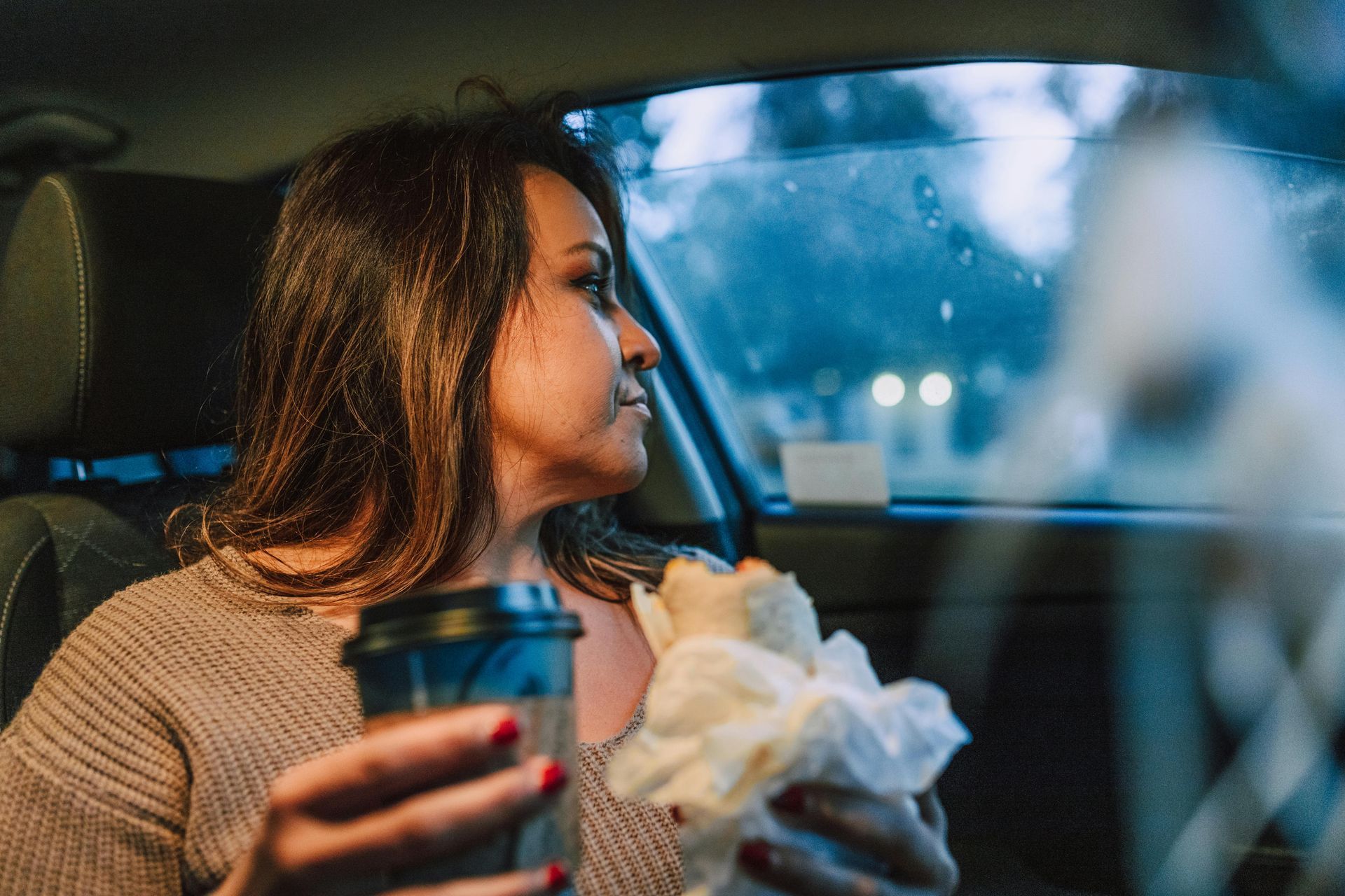 A woman is sitting in the driver 's seat of a car holding a cup of coffee.