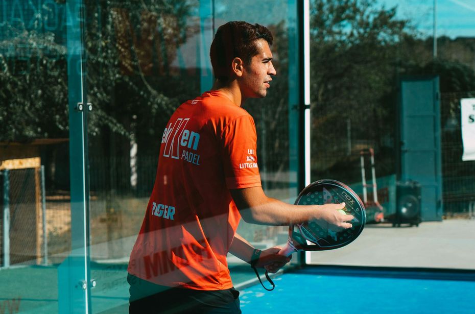 A man in an orange shirt is holding a tennis racquet on a tennis court.