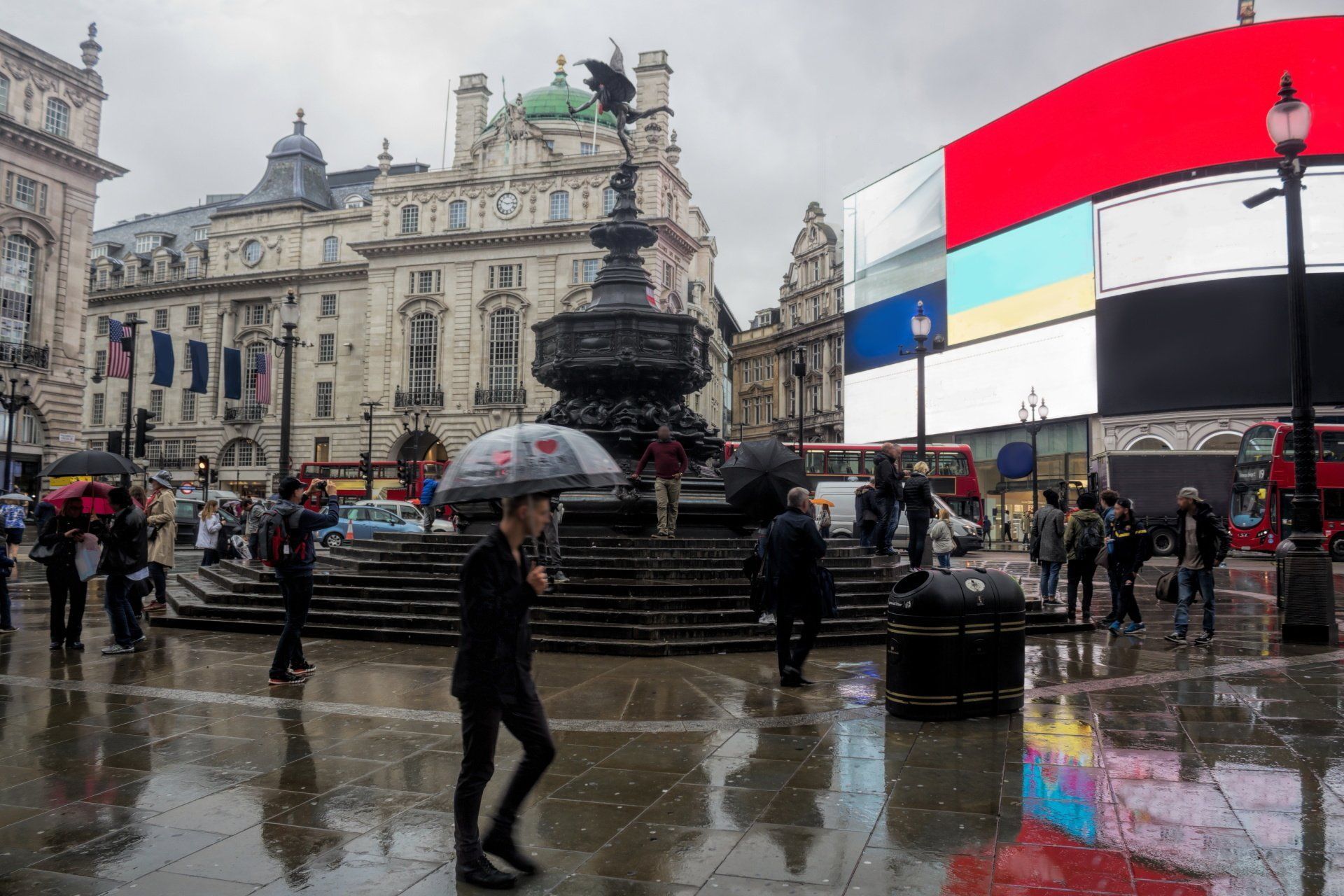 Piccadilly Circus, London on a rainy day; people walk near the Eros statue. 