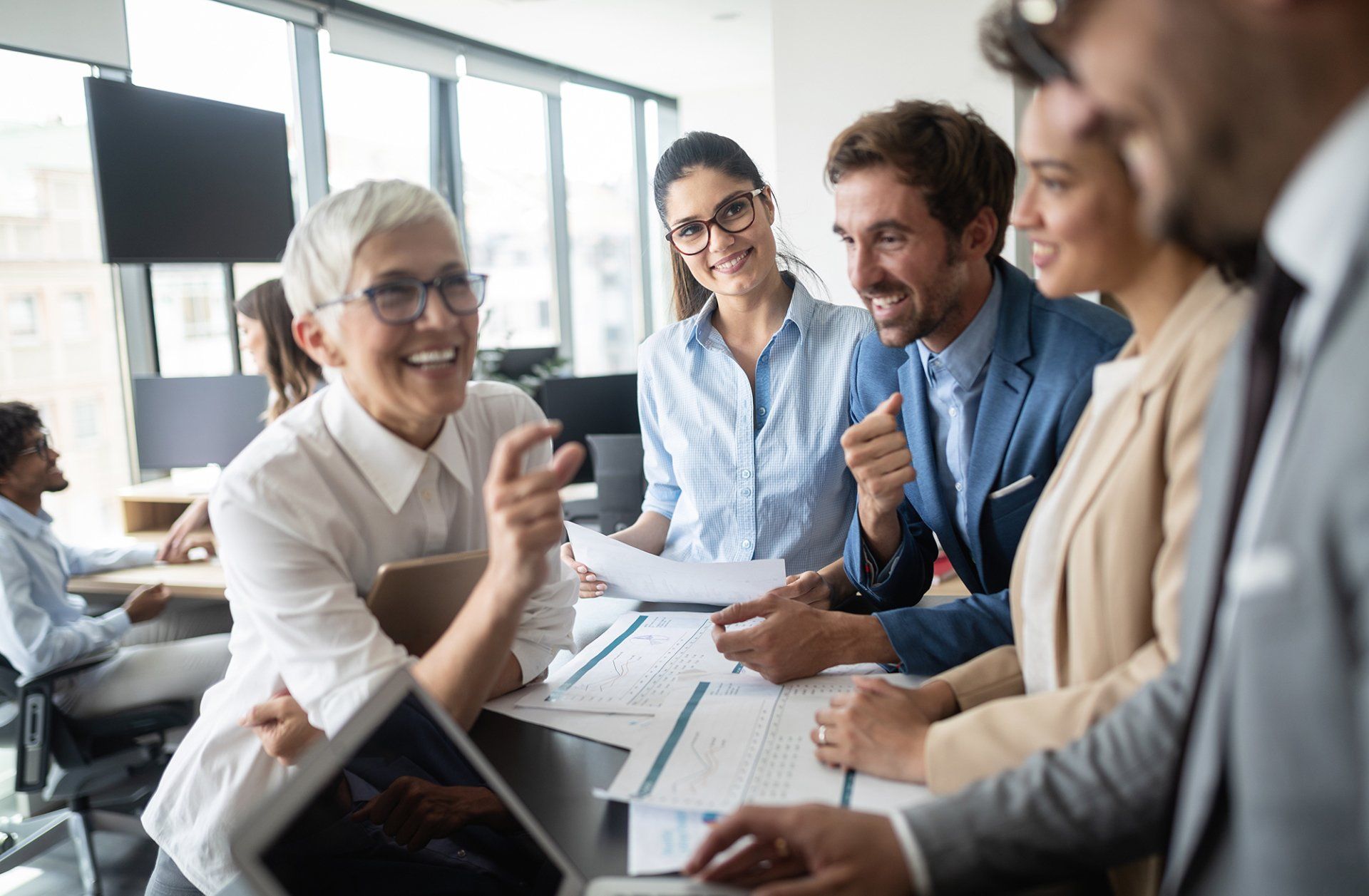 Business colleagues at a desk discussing papers, smiling in a modern office.