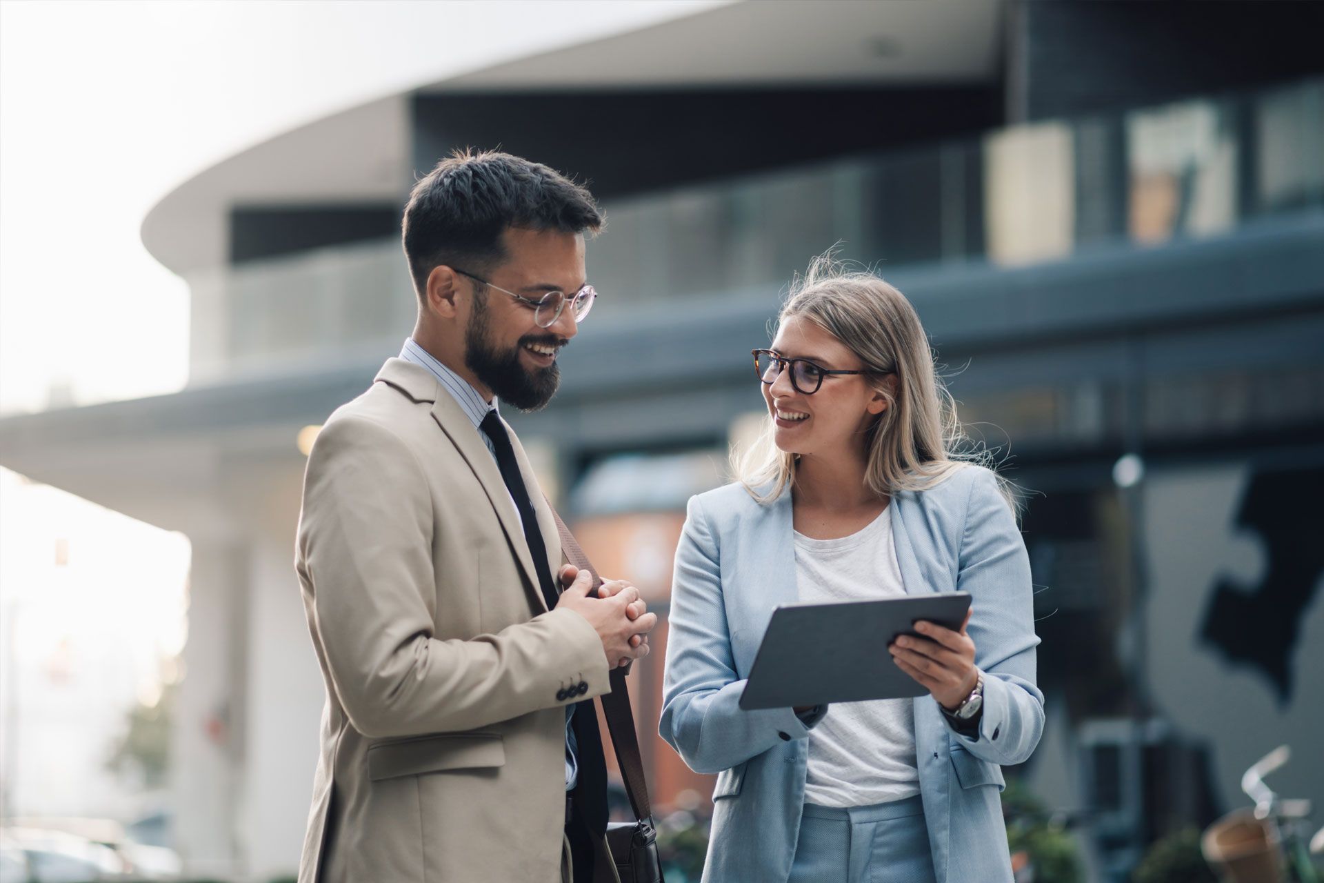 Man and woman in business attire discussing using a tablet outdoors.