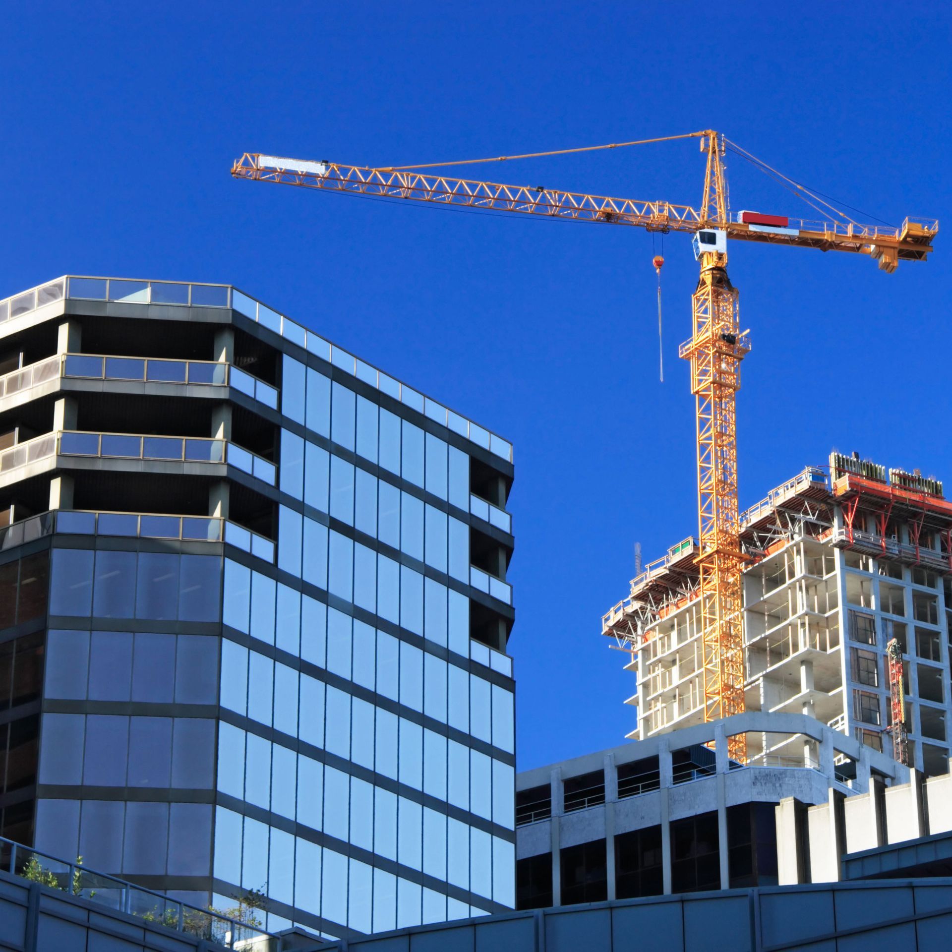 Construction site with crane and modern buildings against a bright blue sky.