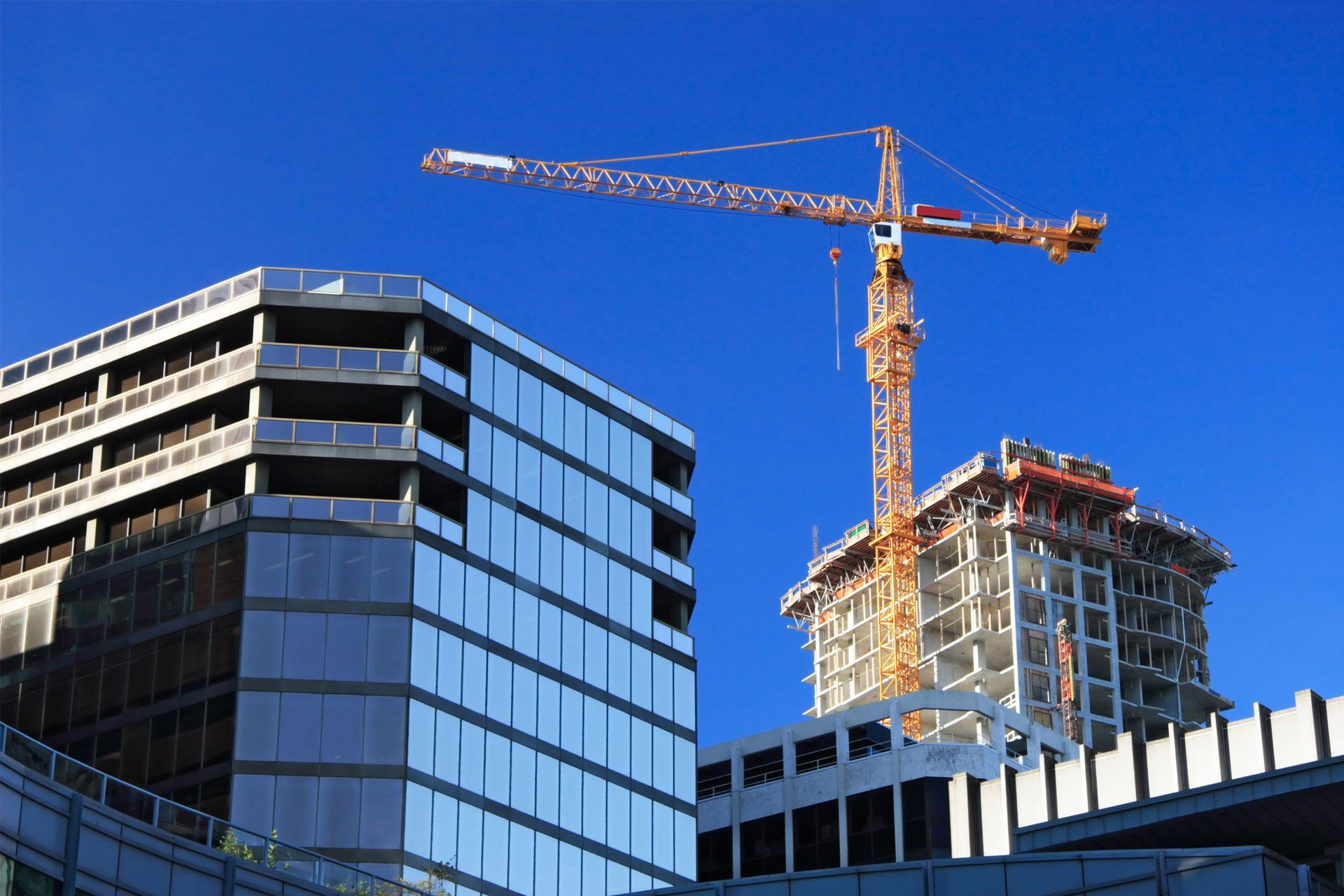 Construction site with a crane lifting materials on a sunny day; partially built buildings.