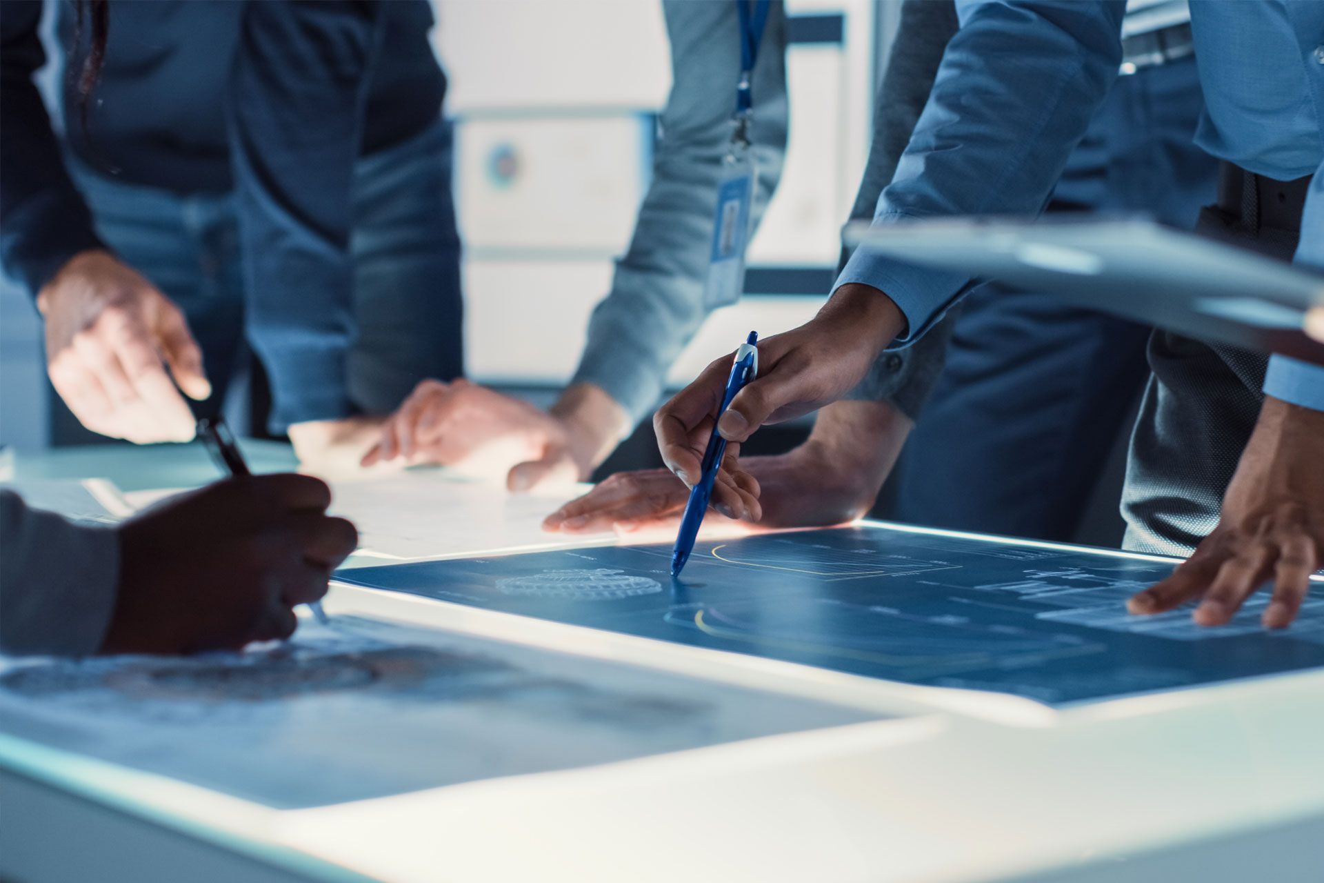 People gather around a light table, pointing at a map and writing with pens.