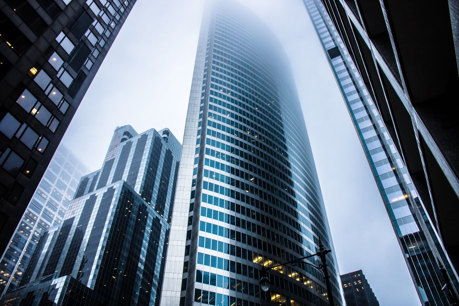 Tall skyscraper, partly obscured by fog, viewed from street level, surrounded by other buildings.