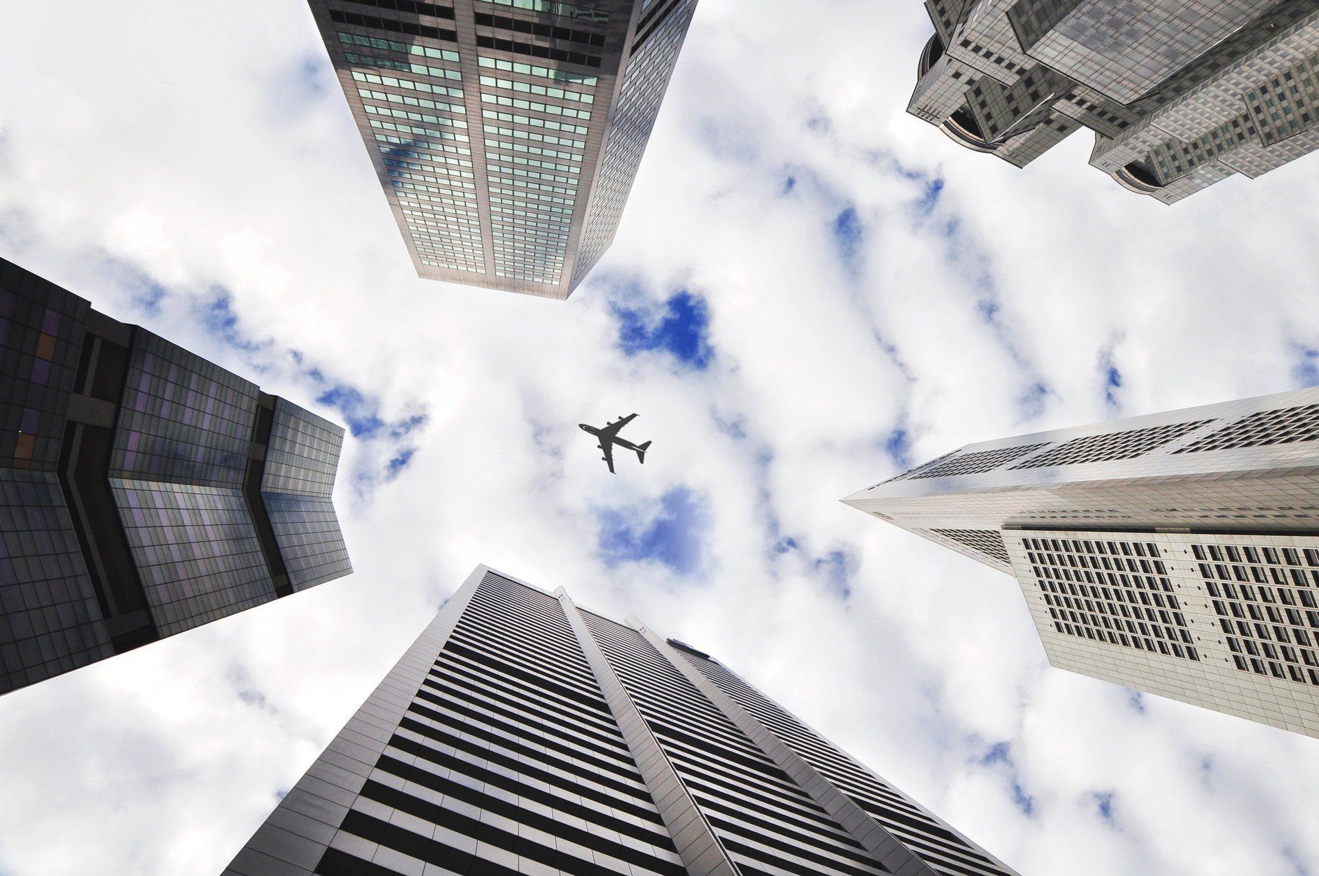 Skyscrapers frame view of the sky and a small airplane.