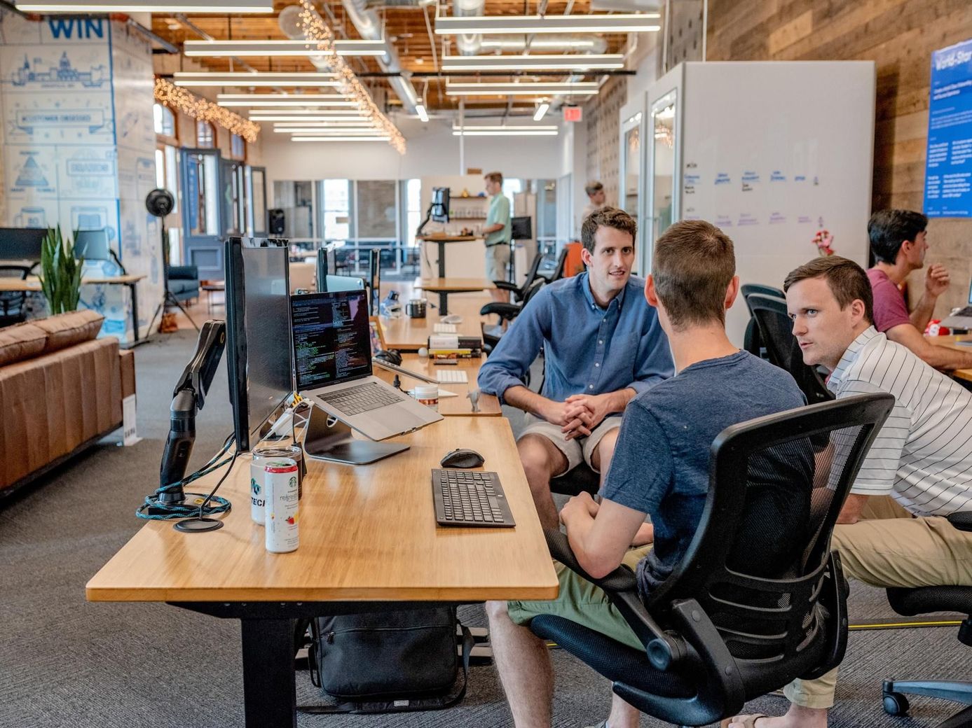 Three men in casual wear collaborate at a desk in a modern office.