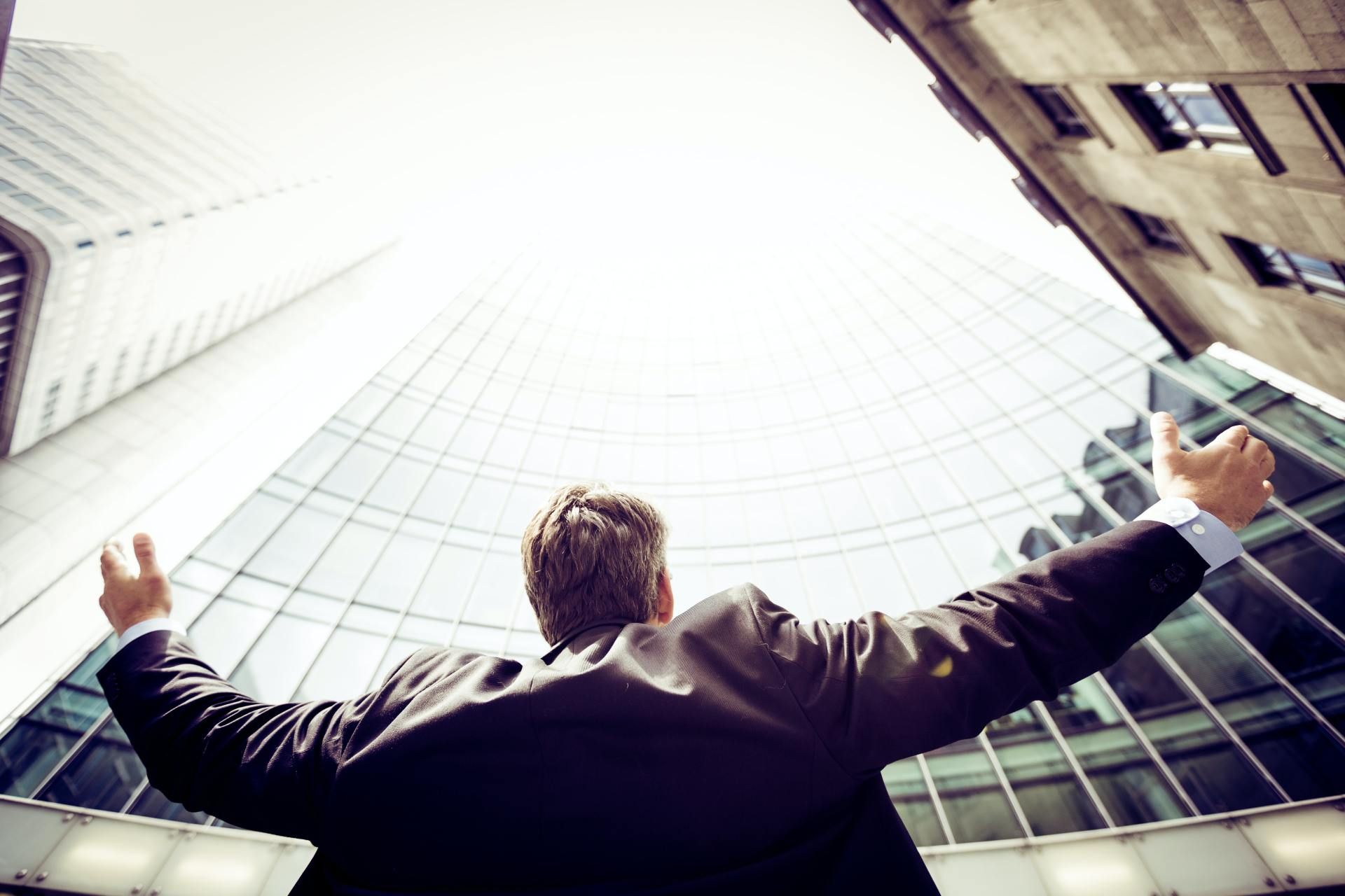 Man in suit with arms raised looking up at skyscrapers.