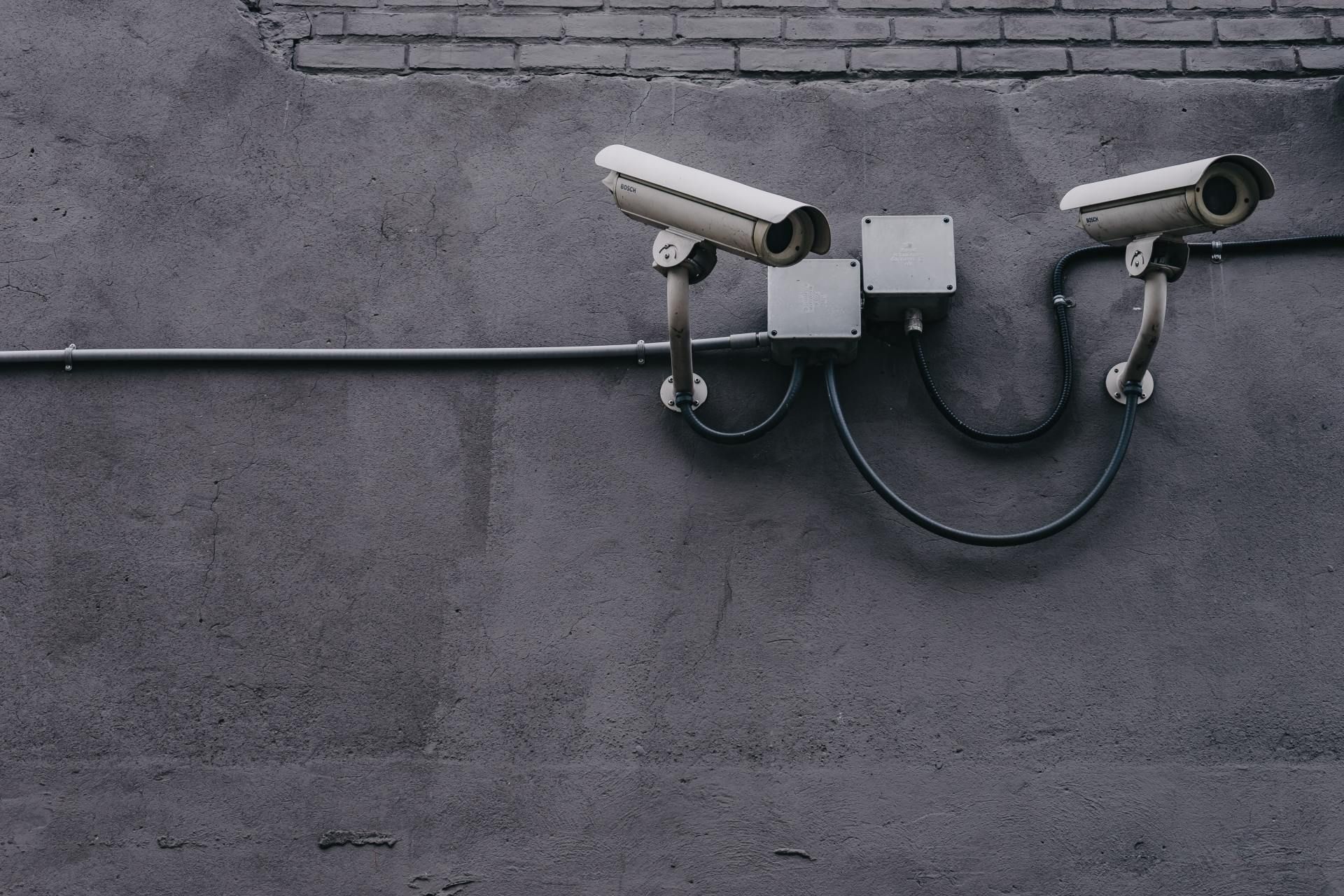 Two security cameras mounted on a gray concrete wall, with a brick section above.