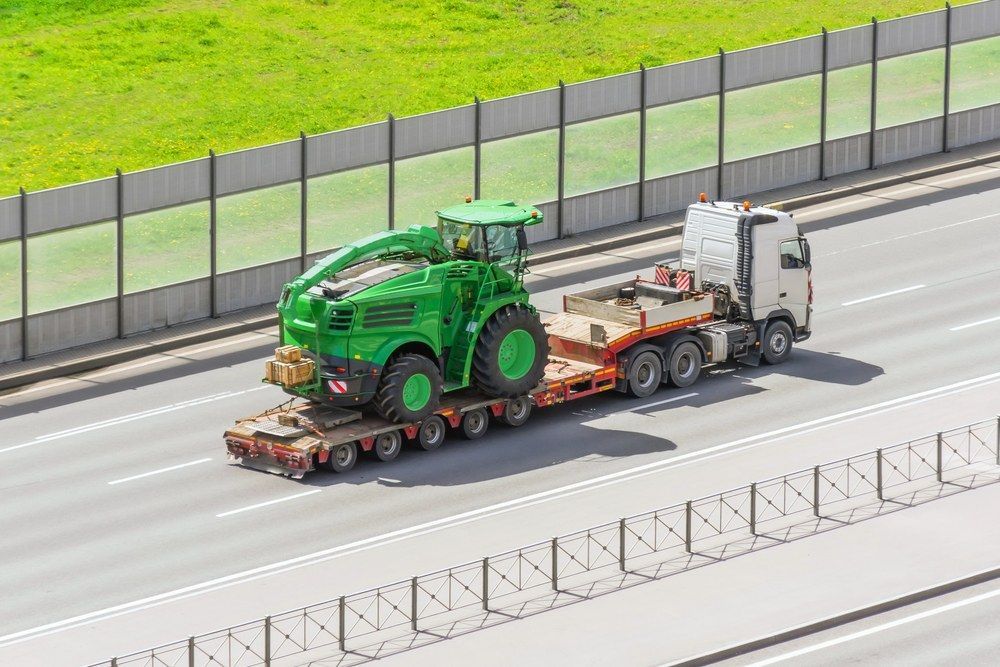 A Green Tractor is Being Transported on a Trailer on a Highway — Jammach Earthmoving in Newcastle, NSW