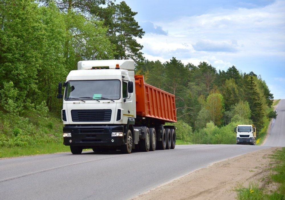 Two Trucks Are Driving Down a Country Road — Jammach Earthmoving in Central Coast, NSW