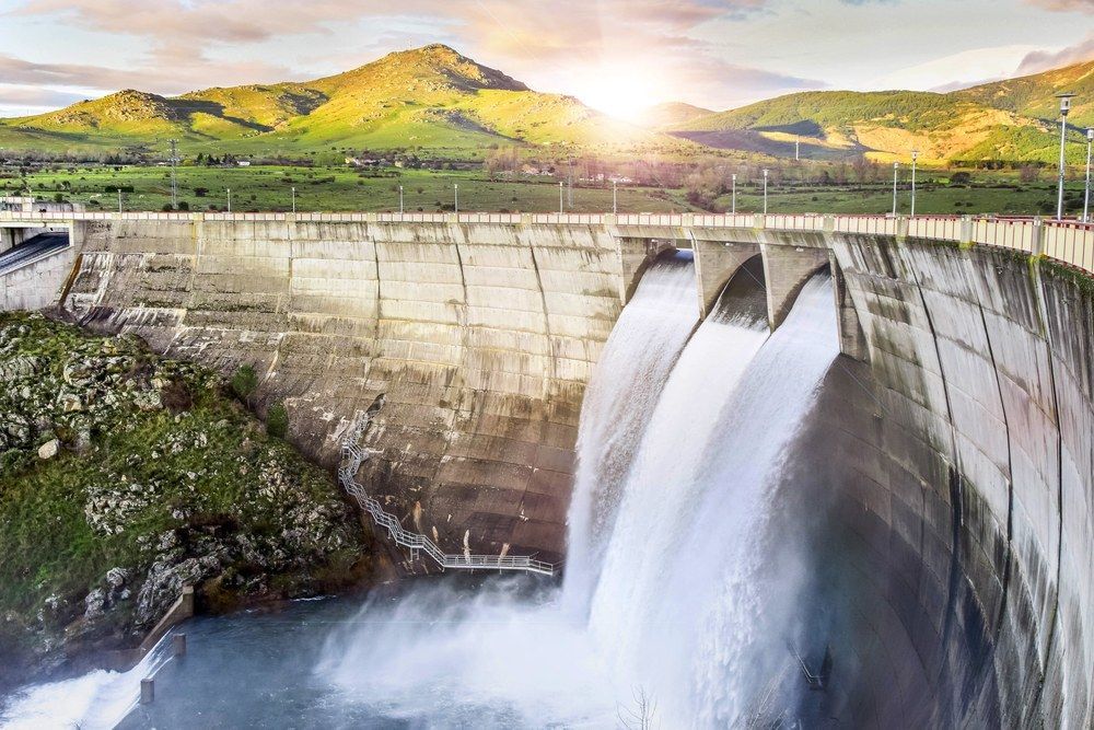 A Waterfall is Coming Down a Dam With Mountains in the Background — Jammach Earthmoving in Maitland, NSW