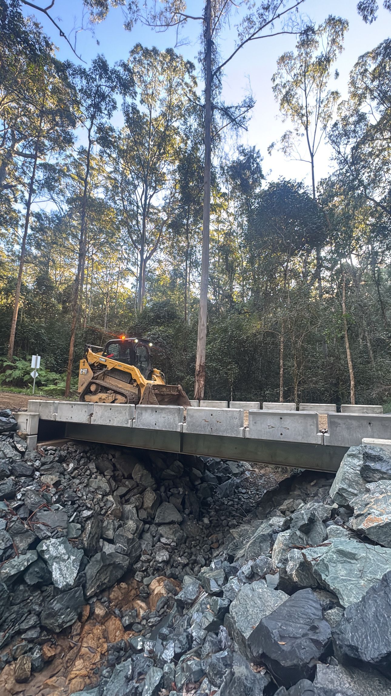 A Bulldozer Is Driving Over A Bridge In The Middle Of A Forest — Jammach Earthmoving in Nulkaba, NSW