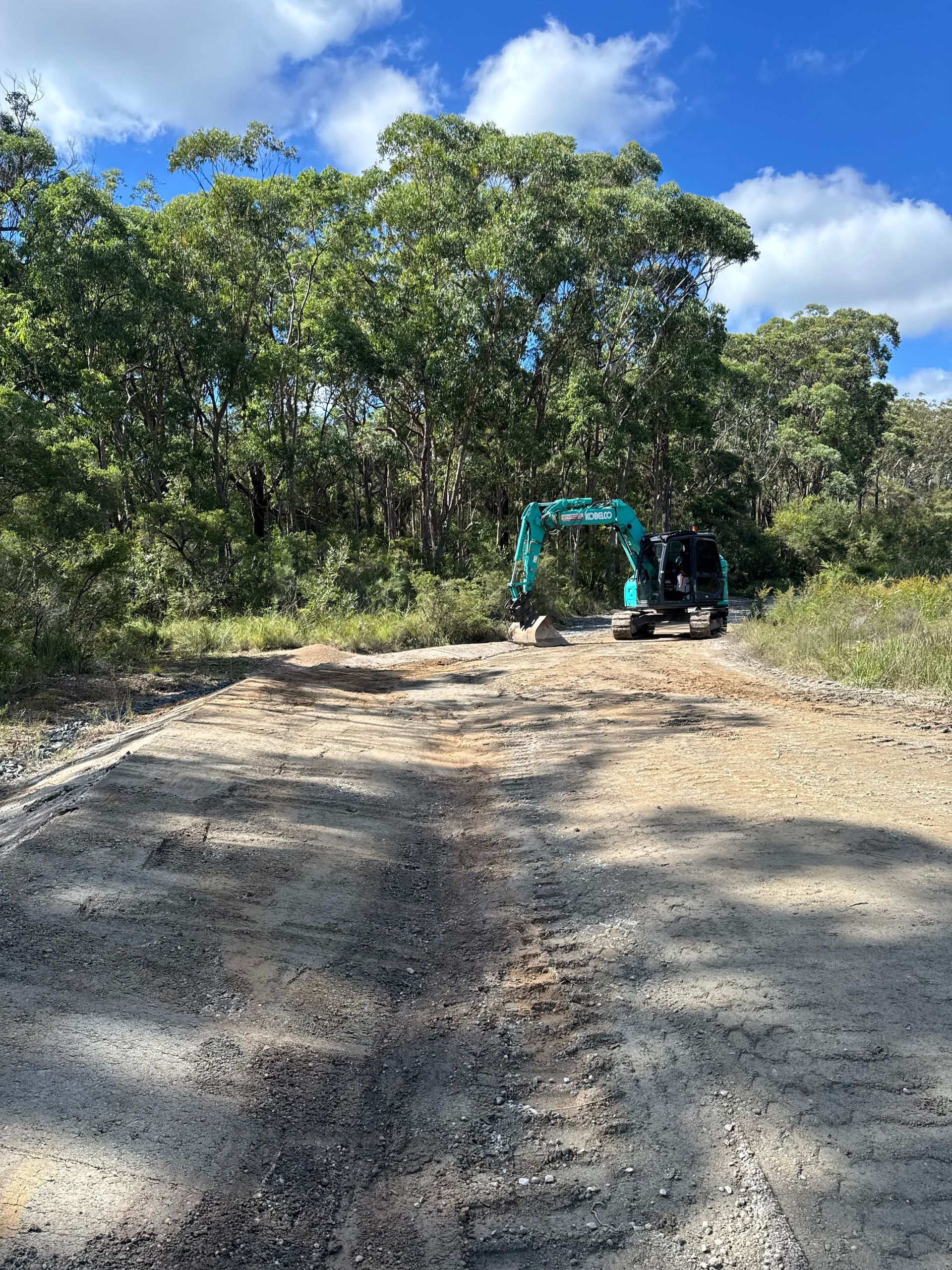 A Blue Excavator on the Dirt in a Dense Forest — Jammach Earthmoving in Nulkaba, NSW