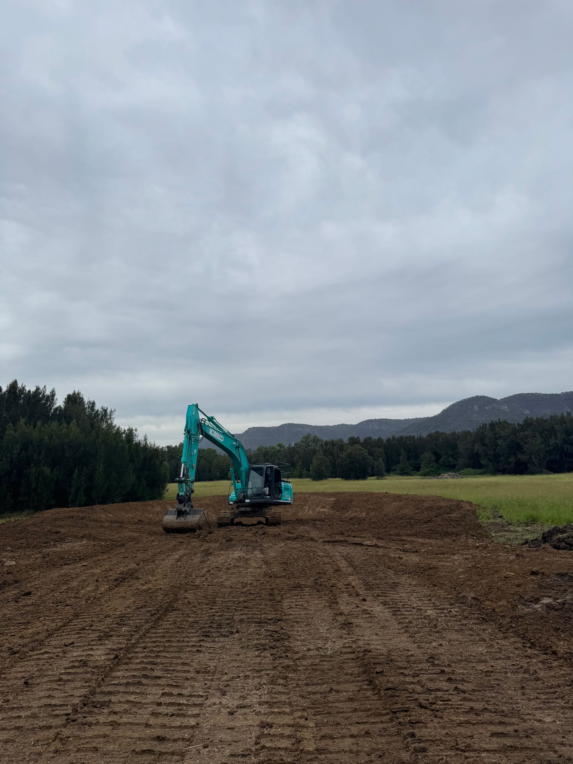 A Blue Excavator is Sitting in the Middle of a Dirt Field — Jammach Earthmoving in Nulkaba, NSW