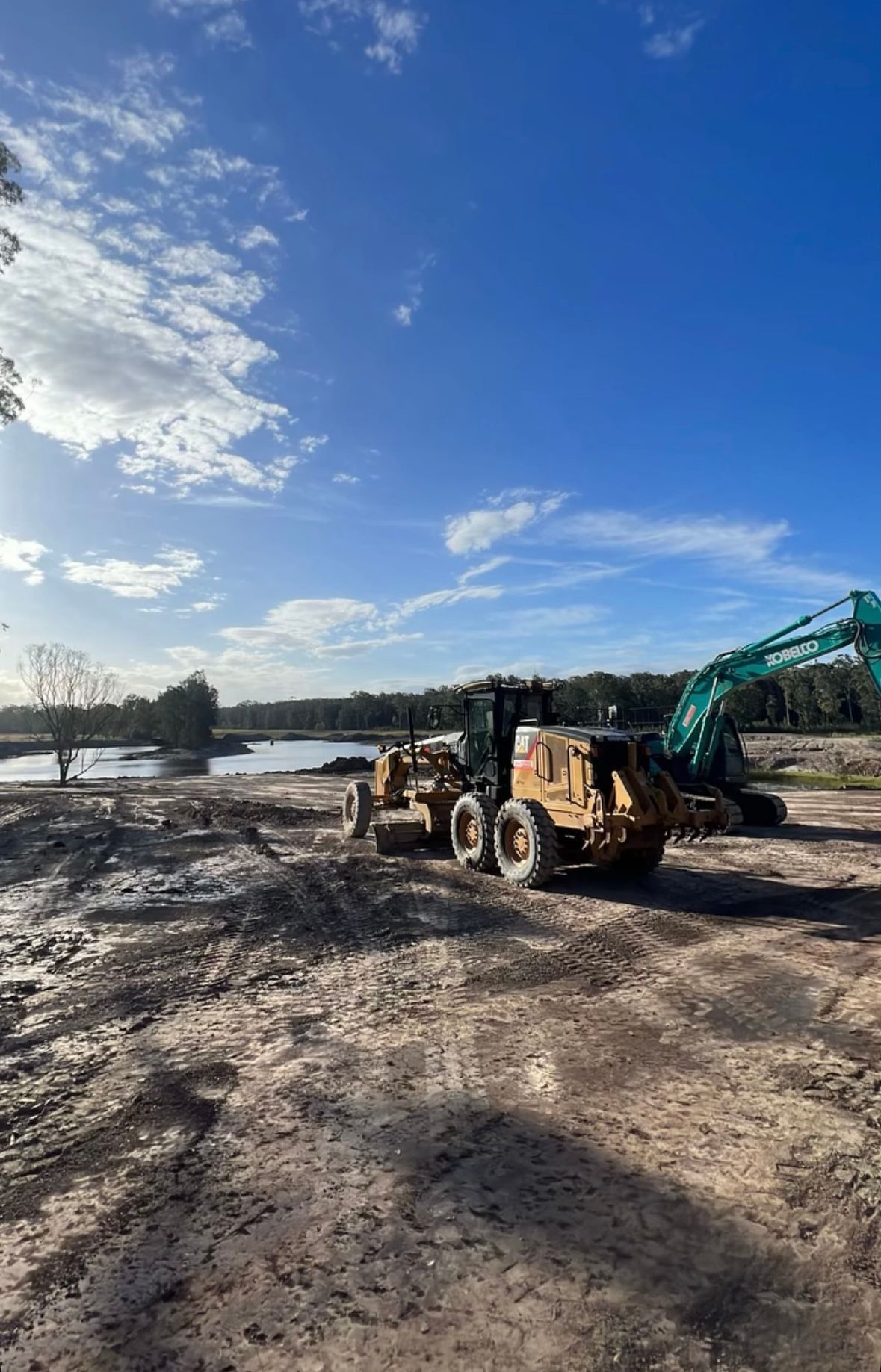 A Couple of Tractors Are Driving Down a Dirt Road Next to a Body of Water — Jammach Earthmoving in Nulkaba, NSW