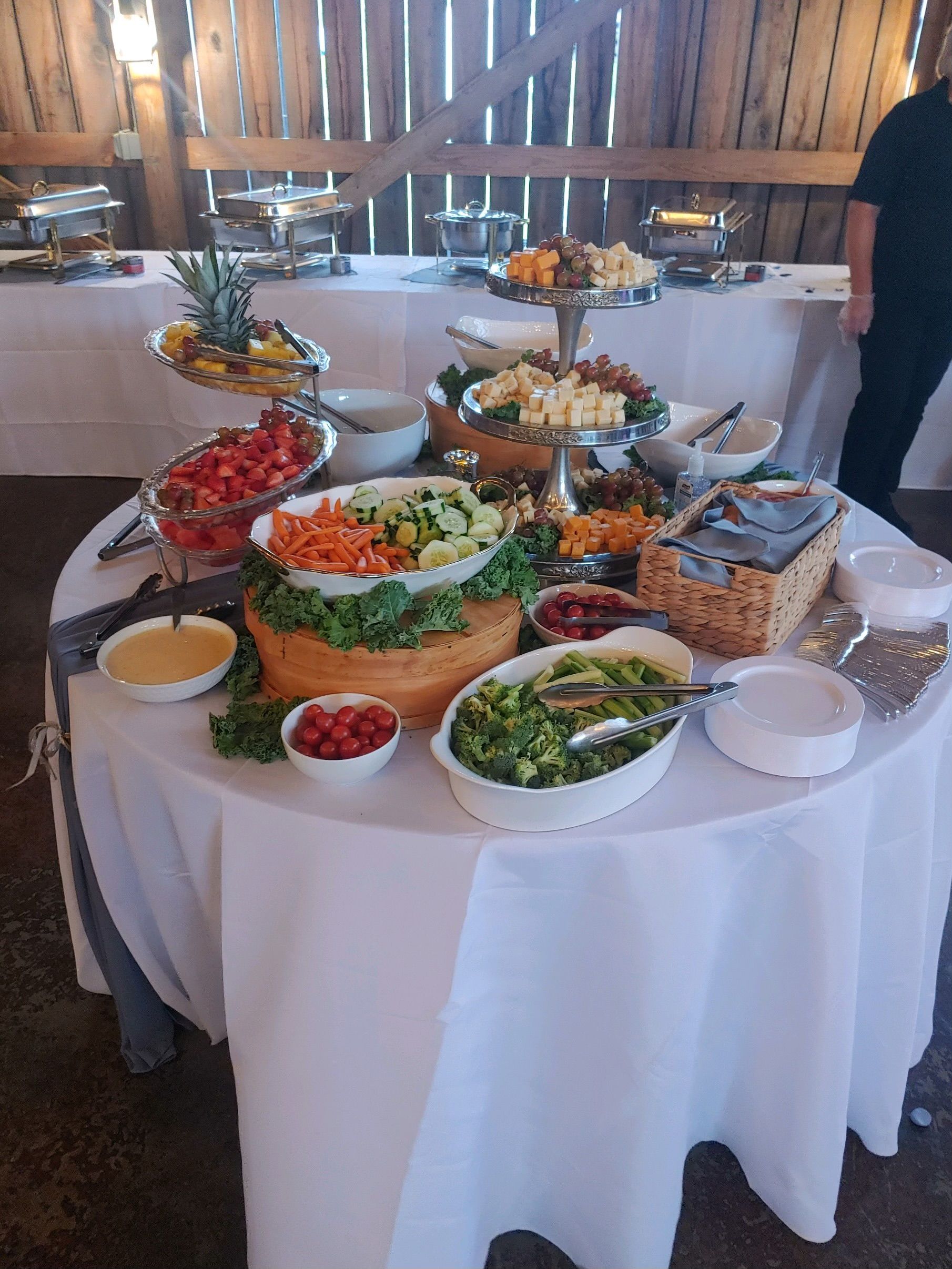 Buffet table with salads, vegetables, and toppings. Placed in a rustic, open space.
