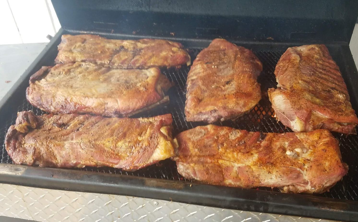 Ribs and pork shoulders grilling on a barbecue, seasoned with a spice rub.