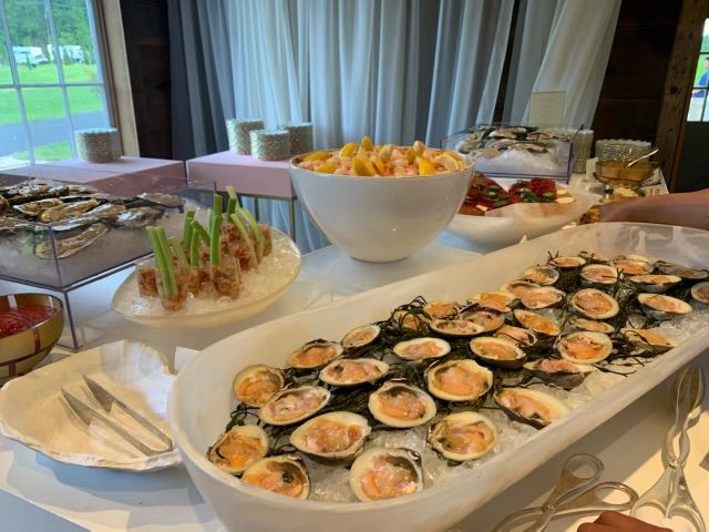 Seafood buffet: oysters, clams, shrimp, and fruit in a room with a window and curtains.