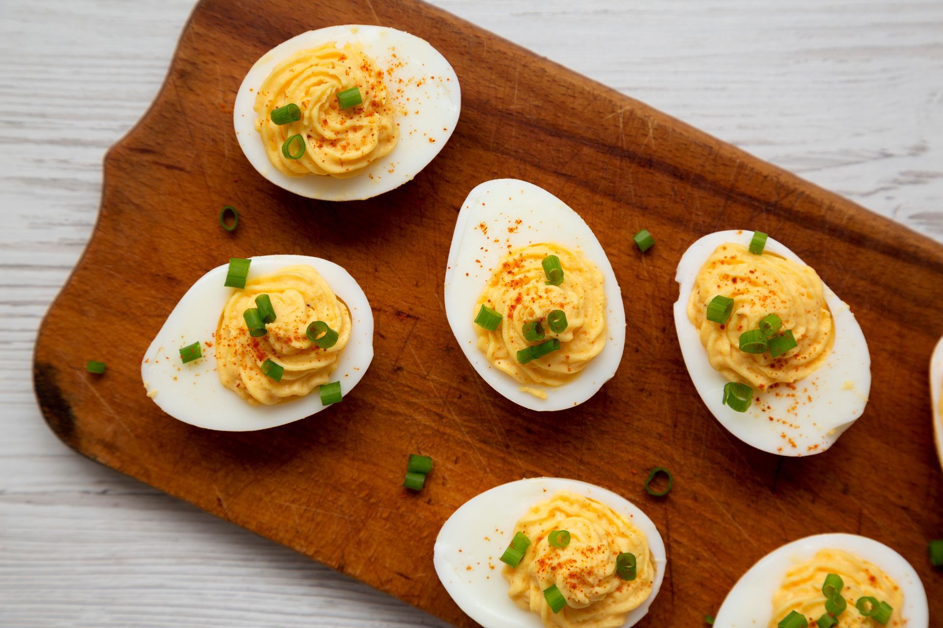 Deviled eggs on a wooden board, topped with paprika and chives.