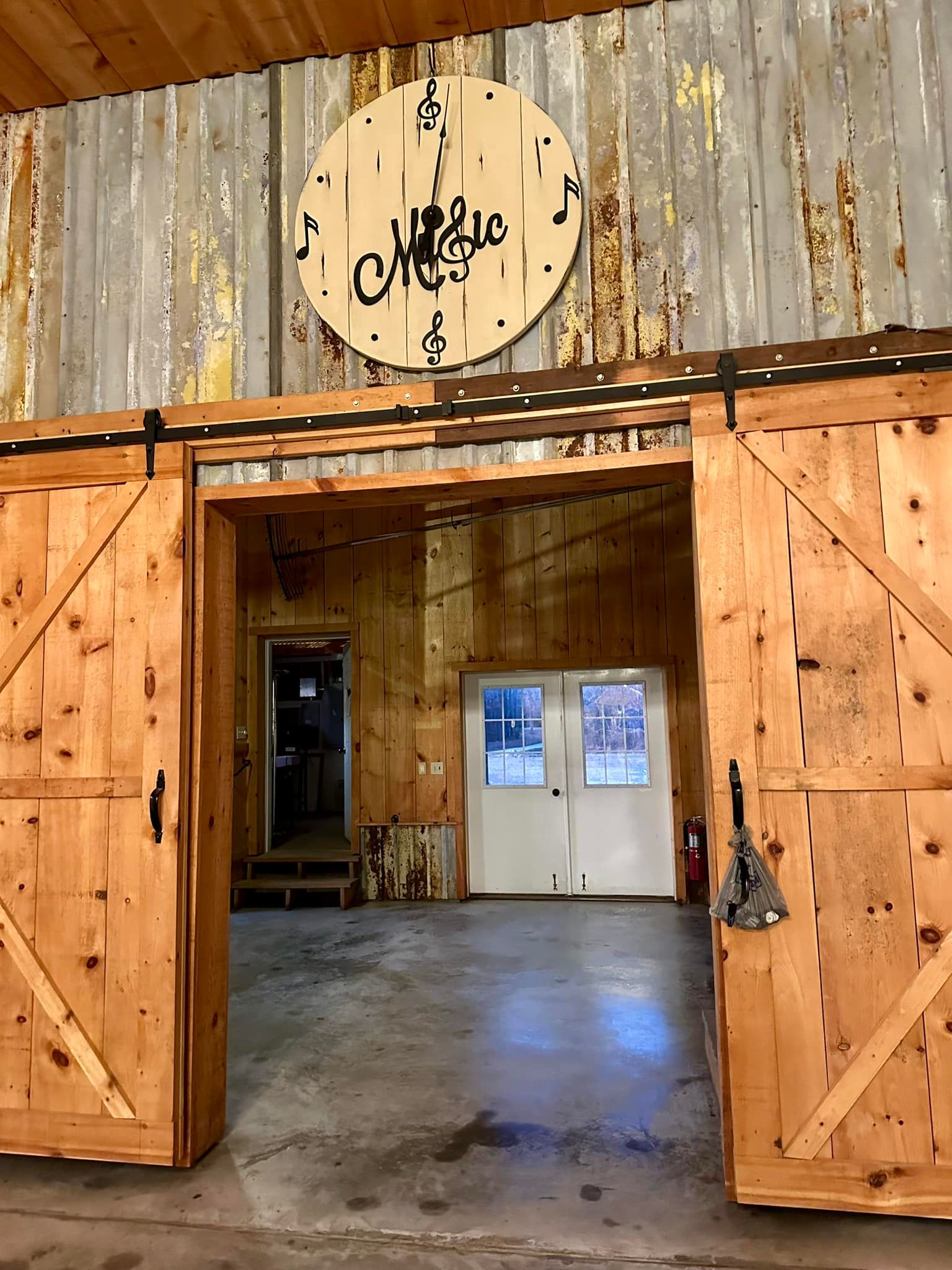 Wooden barn doors open to reveal interior with a clock, wood paneling, and a door.