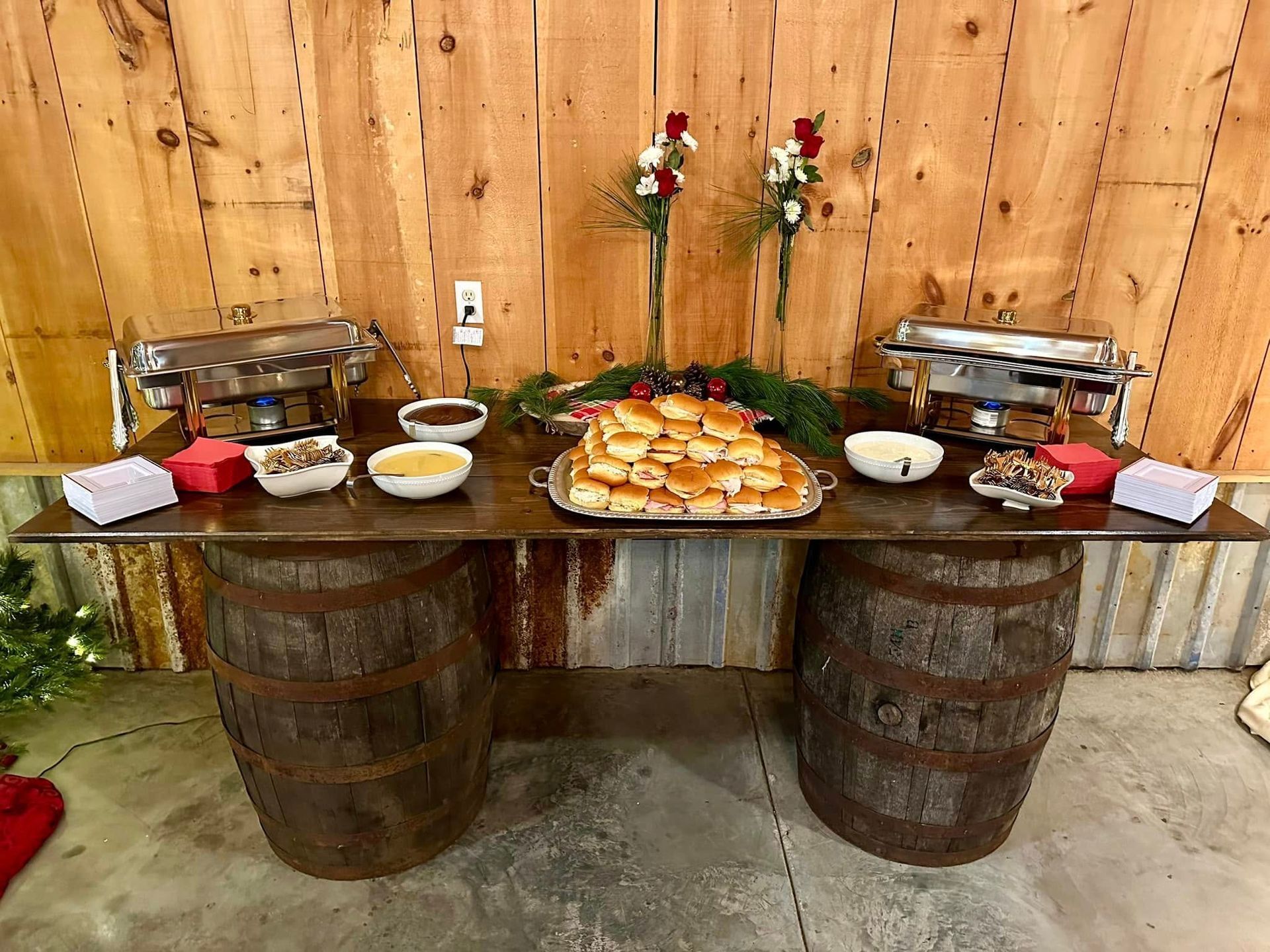 Buffet table on barrels. Food, chafing dishes, and decorations in rustic wooden setting.