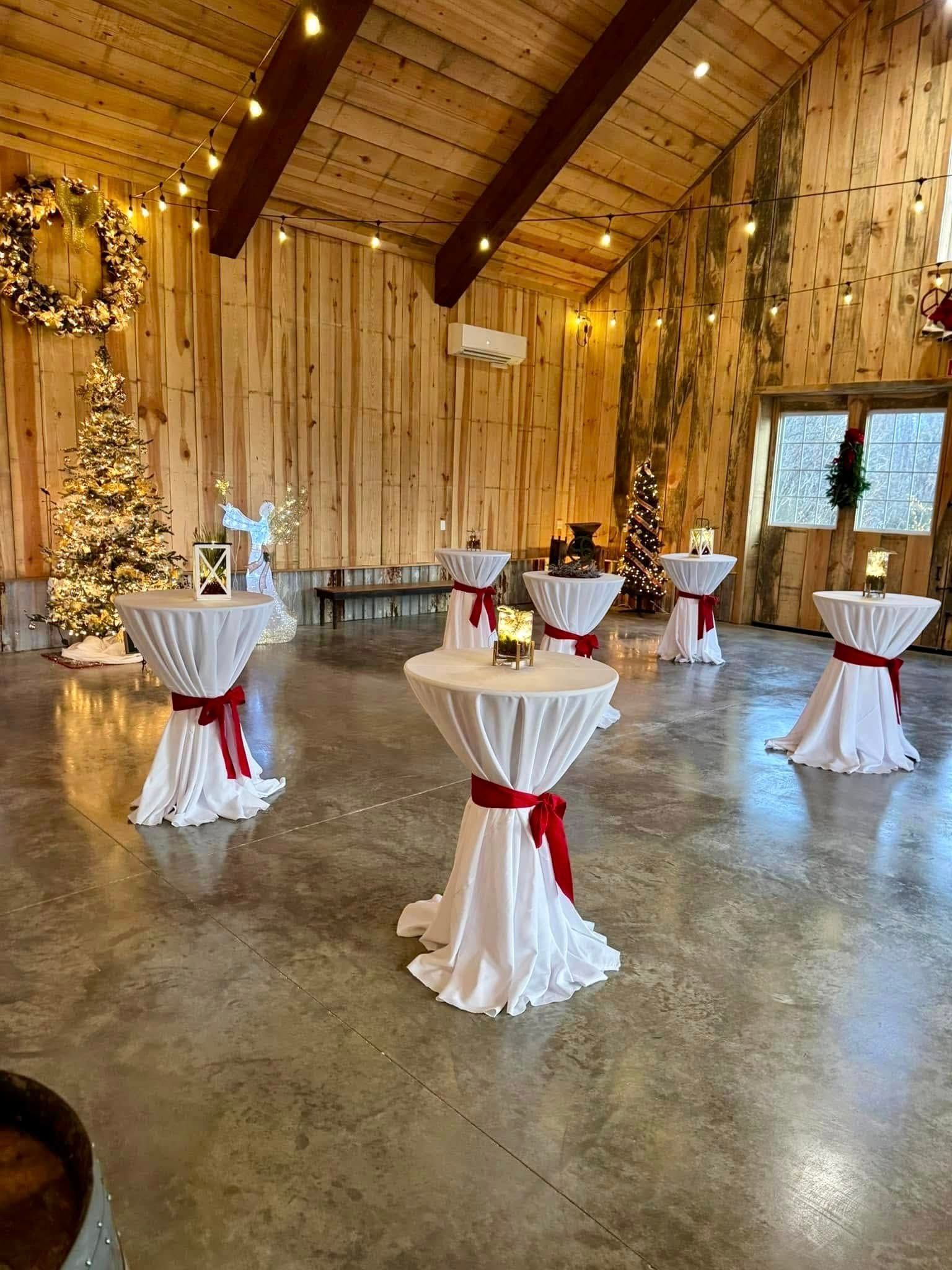 Indoor event space with cocktail tables. White tablecloths with red sashes, Christmas decorations, and wooden walls.