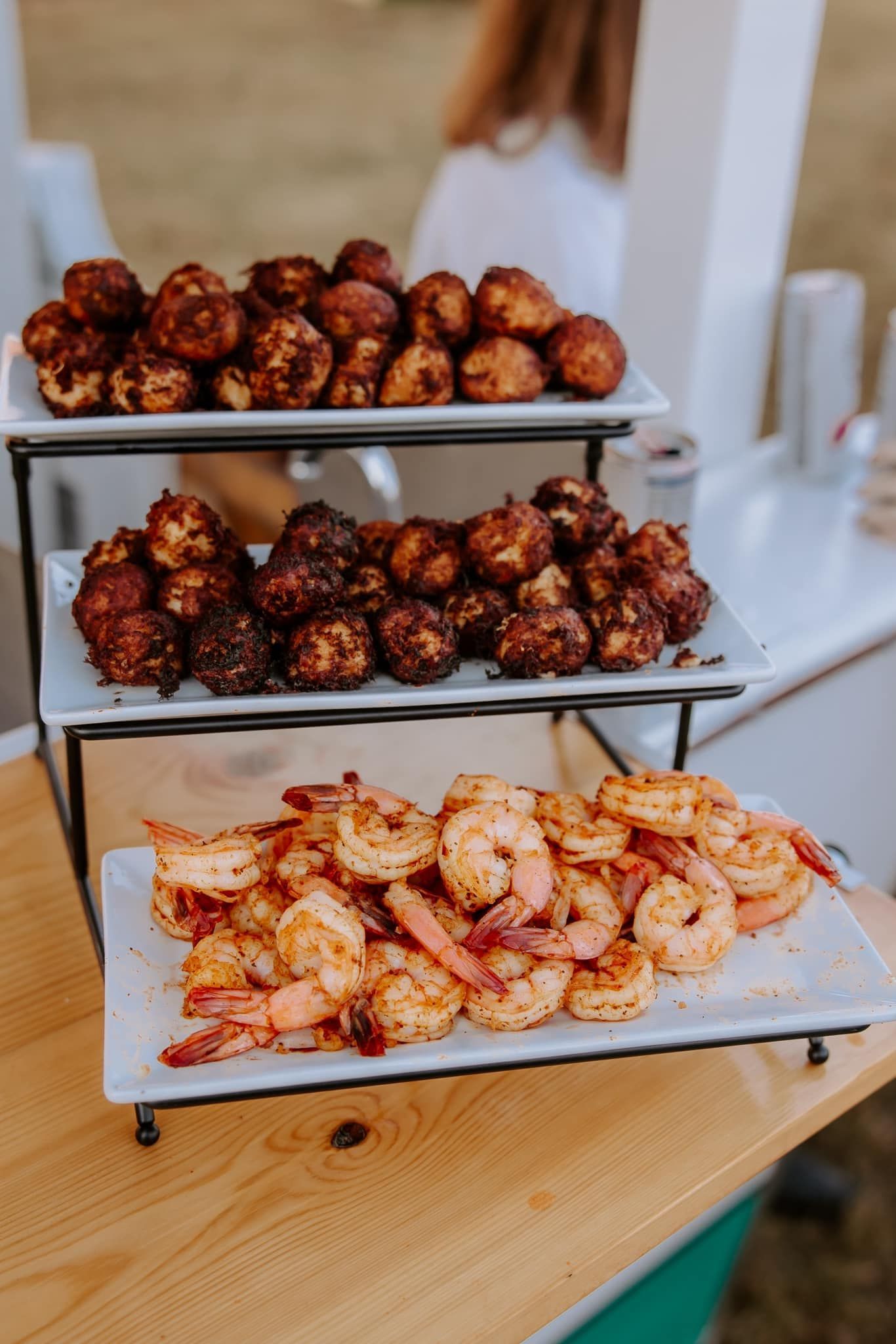 Three-tiered serving stand with fried foods: meatballs, shrimp, and appetizers on a wooden table.
