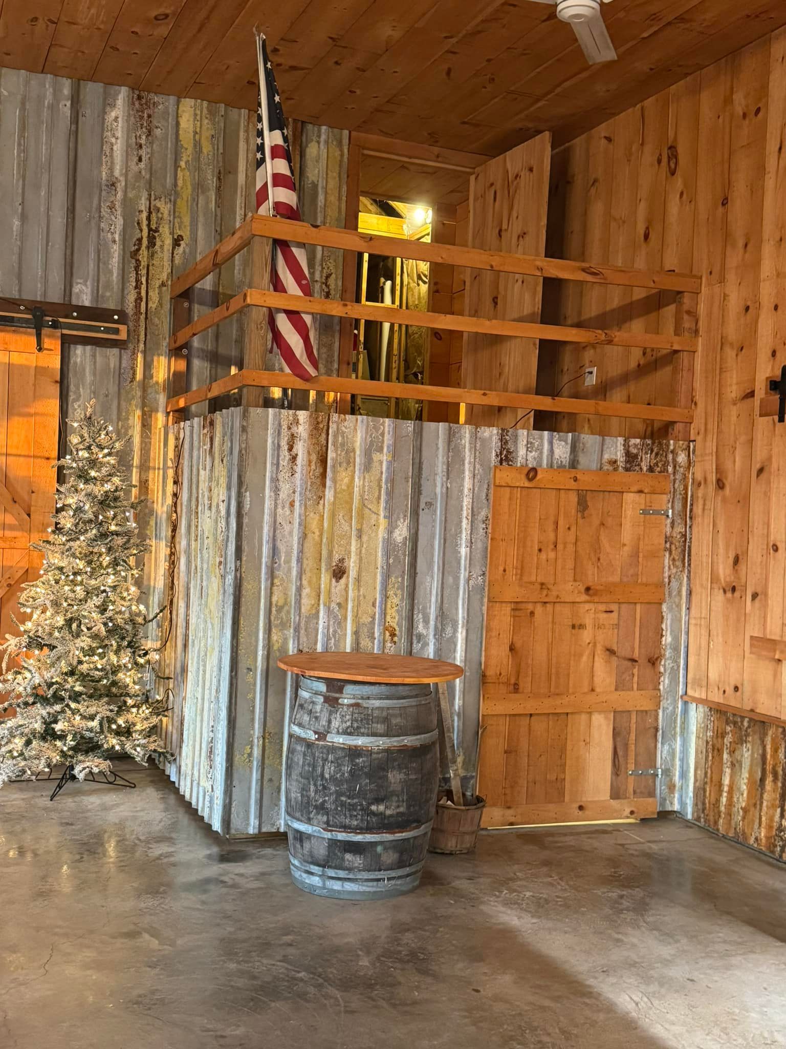 Rustic barn interior with an American flag, barrel table, and Christmas tree.