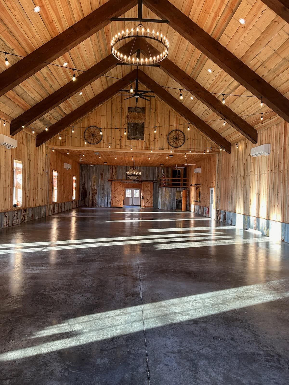 Interior of a spacious wooden barn with concrete floor, a chandelier, and string lights, ready for an event.