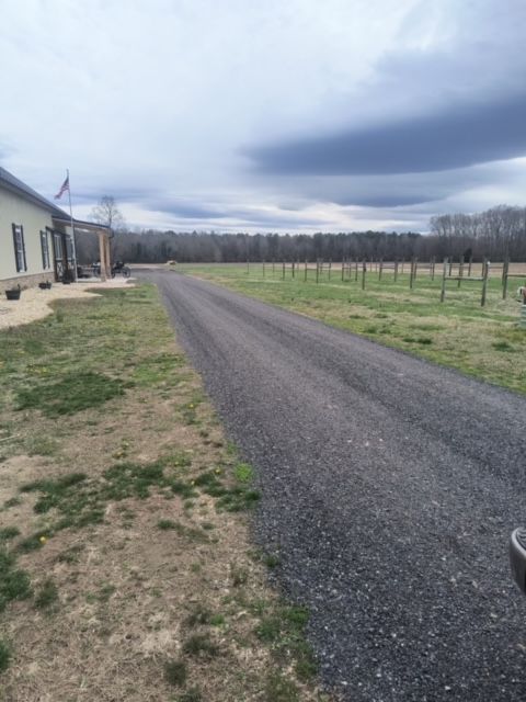 Gravel driveway leads to a house on a cloudy day. Trees are visible in the distance.