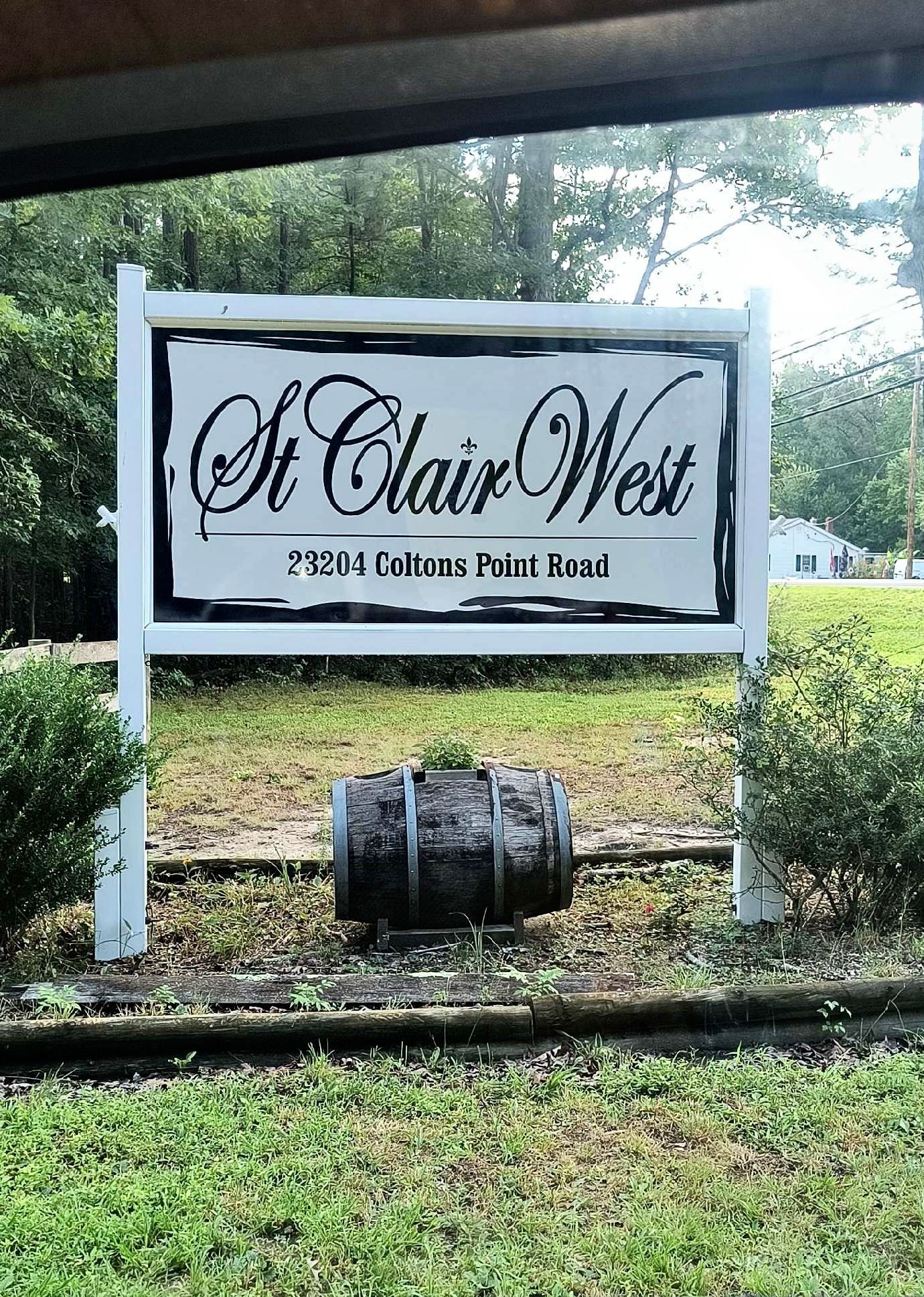 Sign for St. Clair West at 75004 Colton's Point Road; a dark barrel sits below the sign, surrounded by greenery.