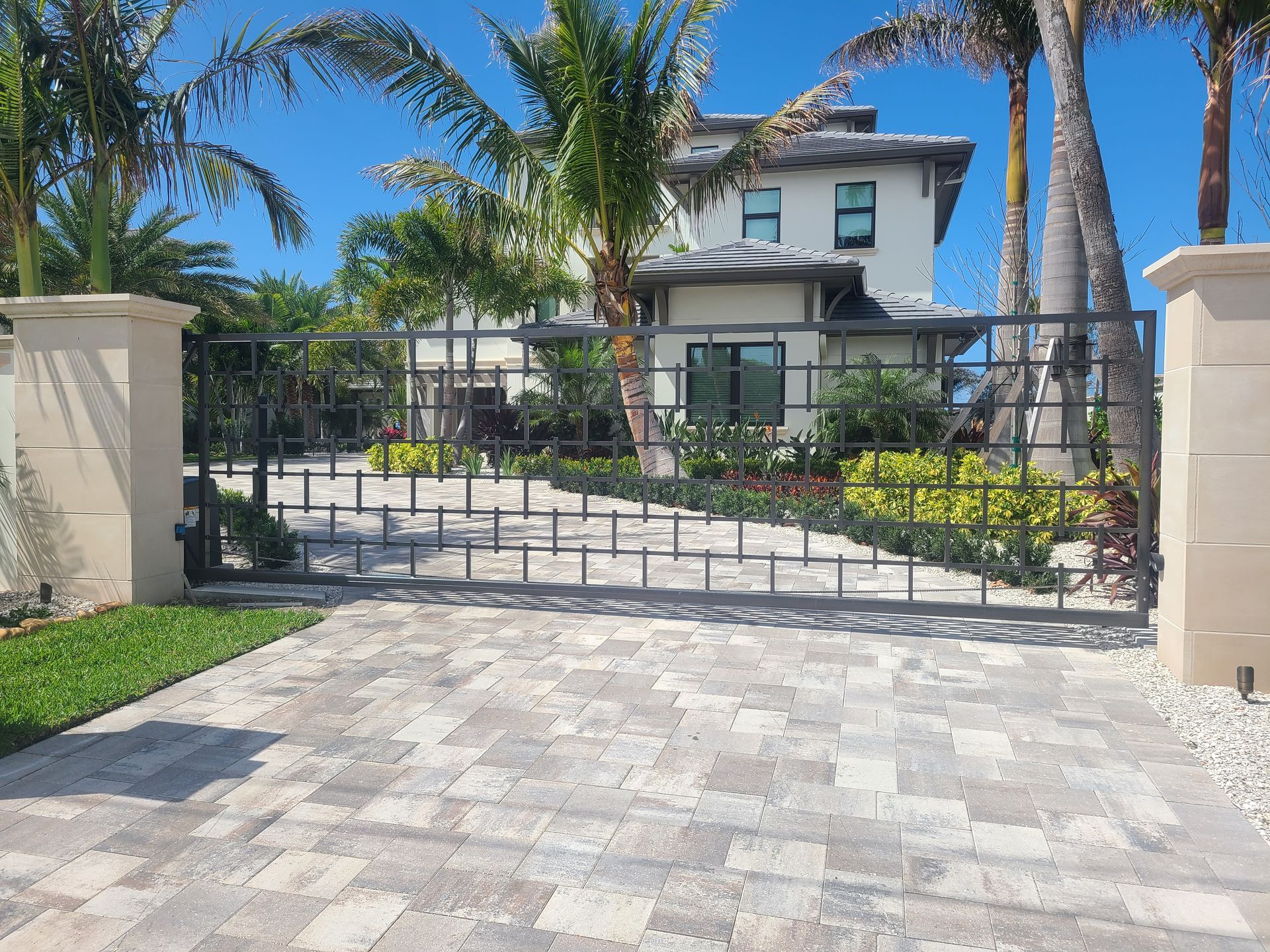A large house with a gated driveway and palm trees in front of it.