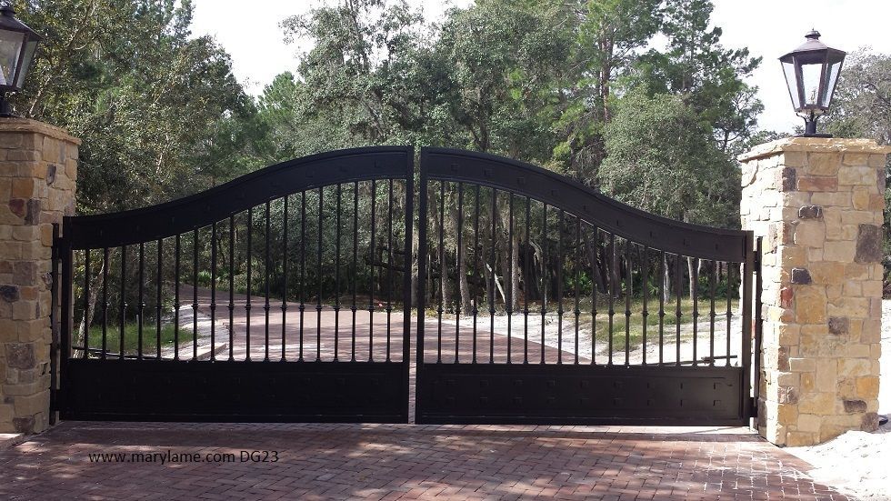 A black wrought iron gate is surrounded by stone pillars and trees.