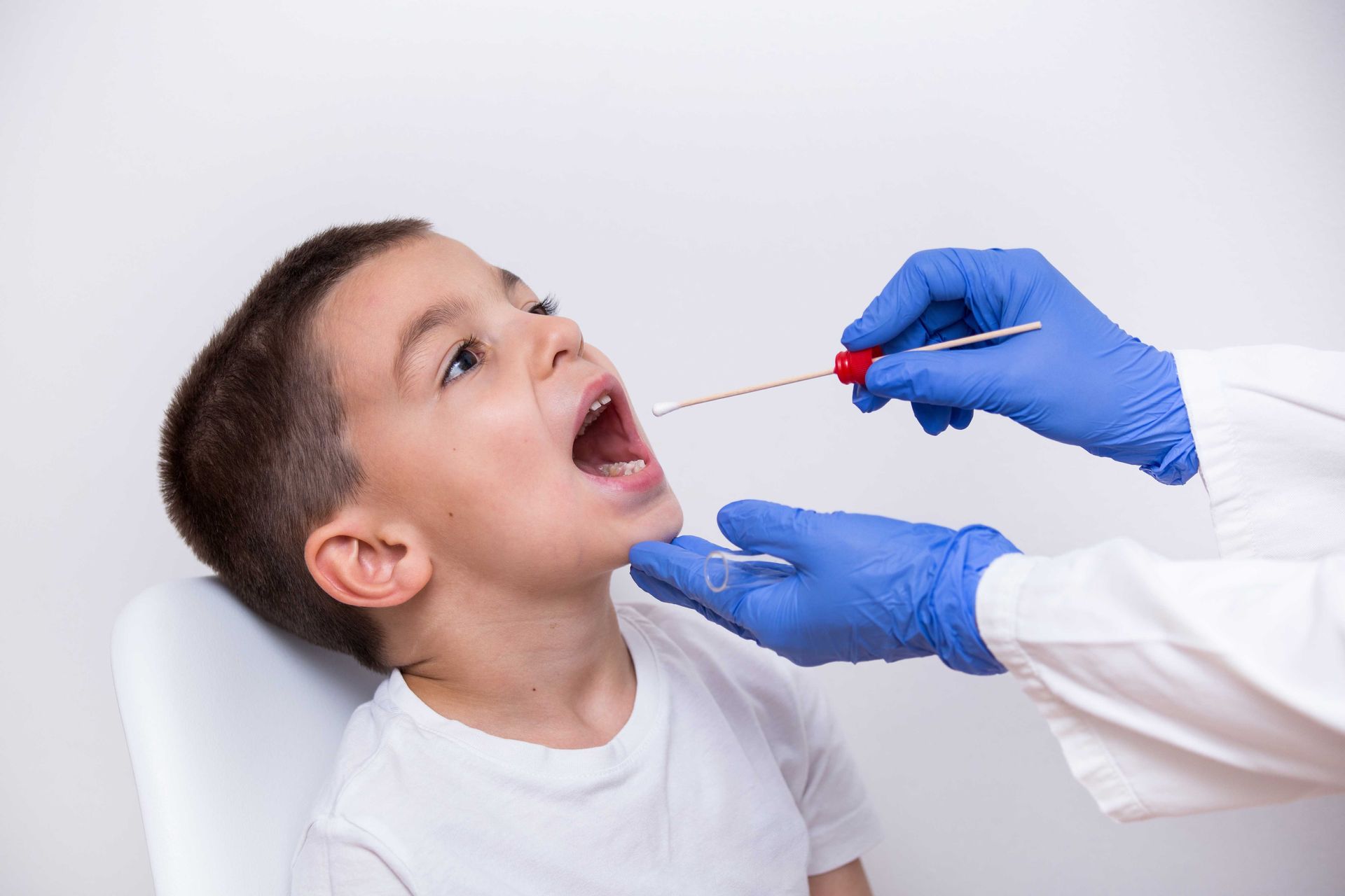 Doctor's hands in gloves using a cotton swab to test a young boy for bacterial infections Doctor's hands in gloves using a cotton swab to test a young boy for bacterial infections