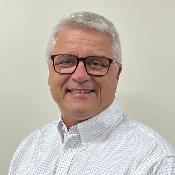 A man wearing glasses and a plaid shirt is smiling for the camera.