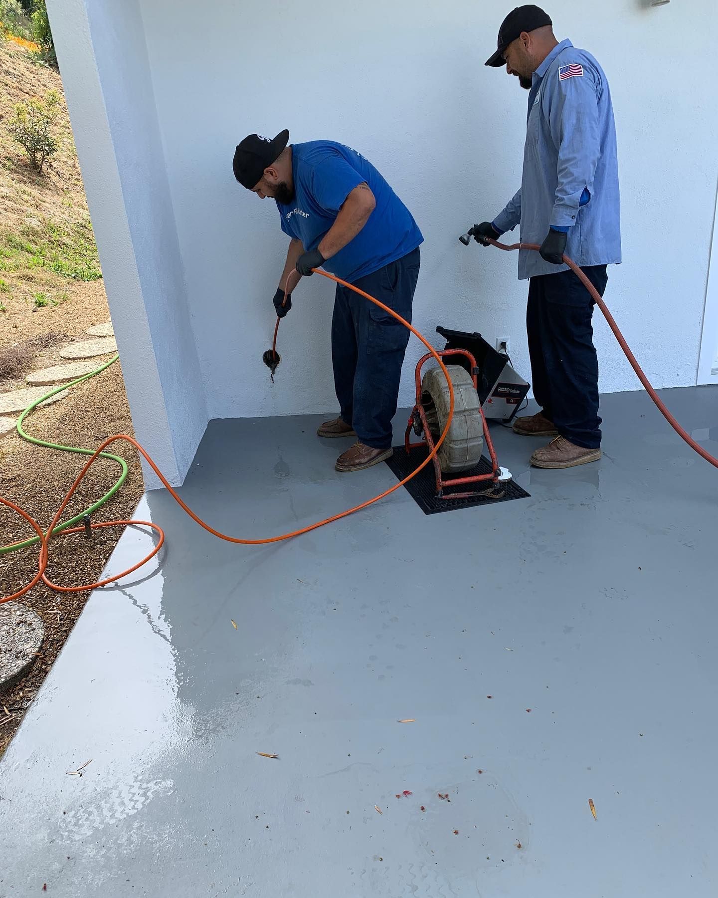 Two men are working on a drain in a room.