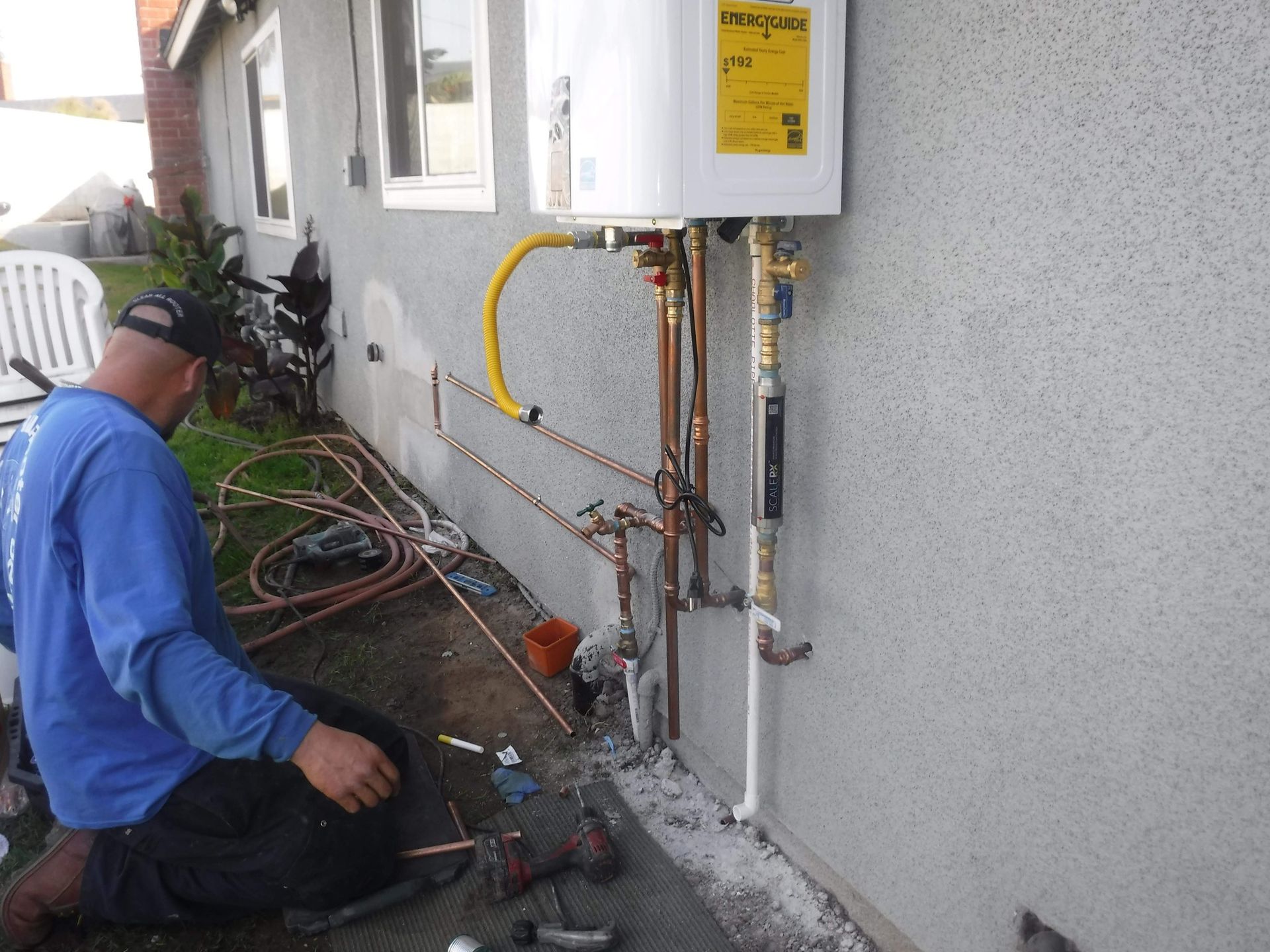 A man is working on a water heater outside of a house.
