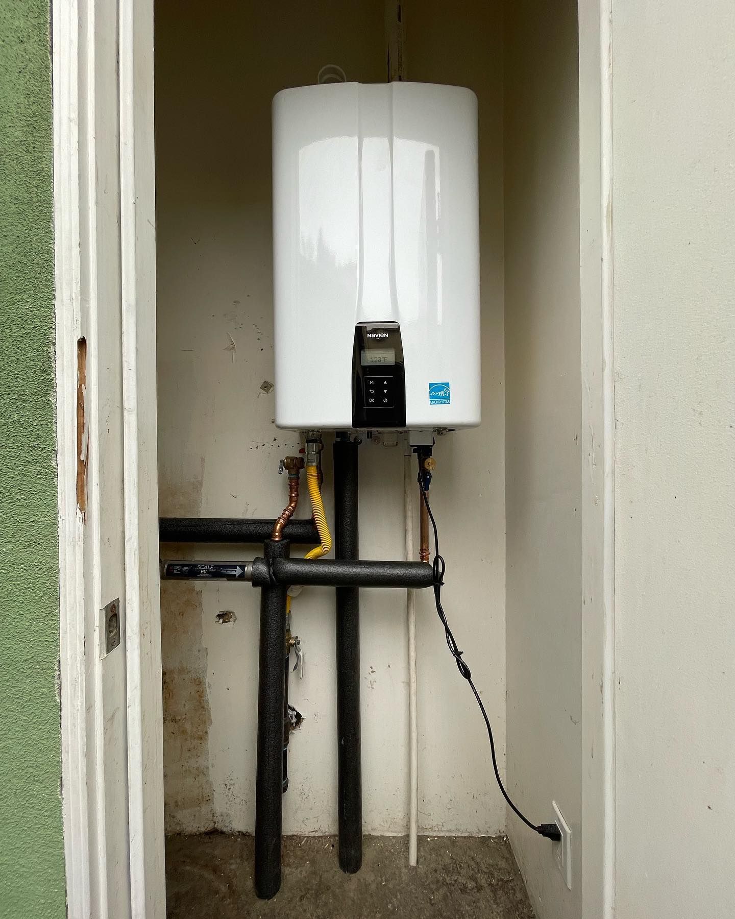 A white water heater is mounted on a wall next to pipes