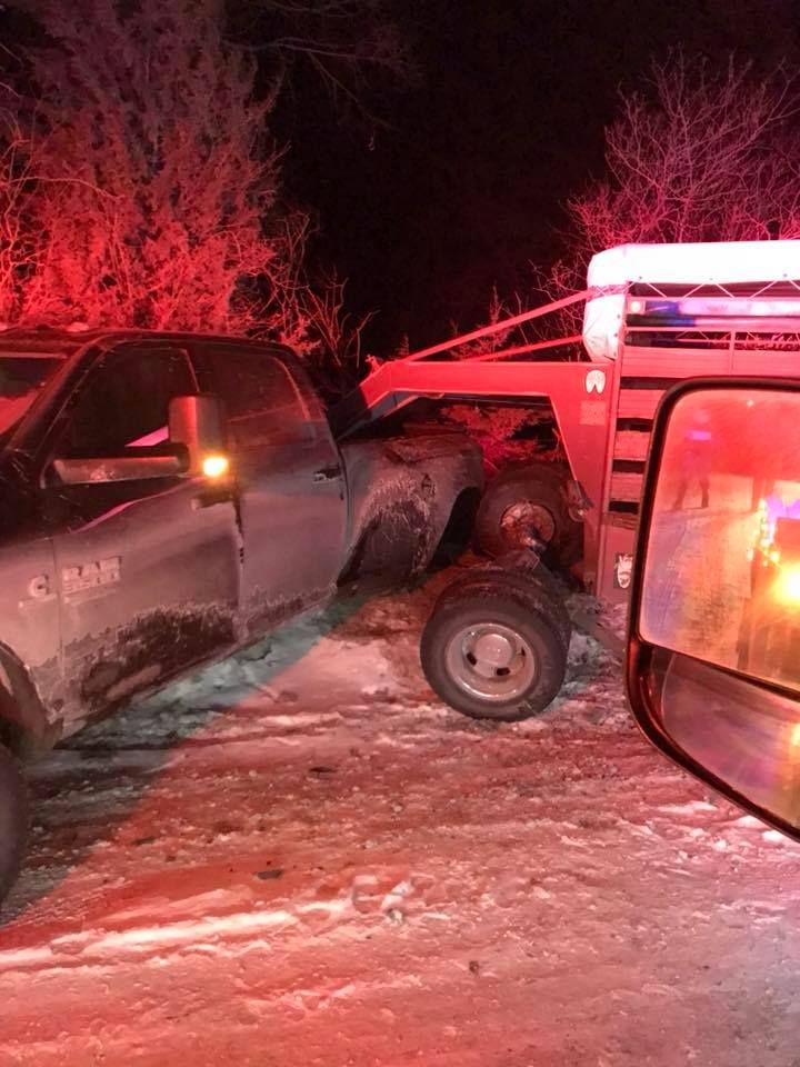 A dark truck towing a damaged red trailer at night. Roadside setting with snow and dim lighting.