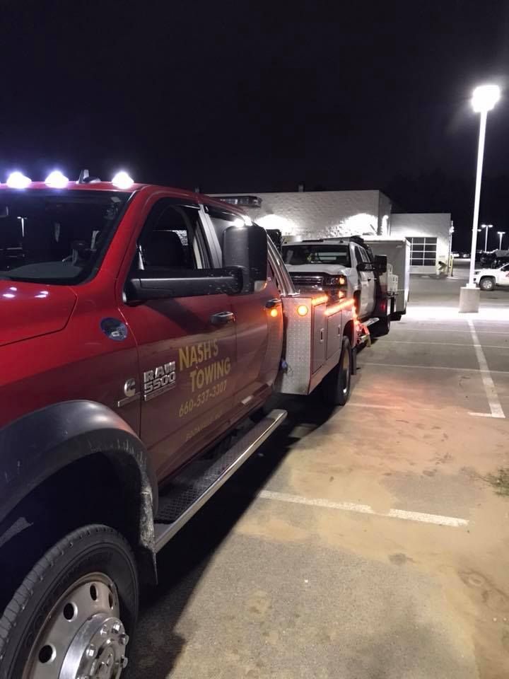 Red tow truck towing a vehicle at night in a parking lot; the tow truck has its lights on.
