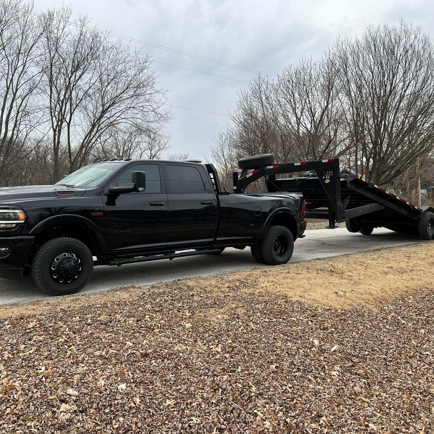 Black pickup truck towing a black trailer on a gravel road, overcast day.