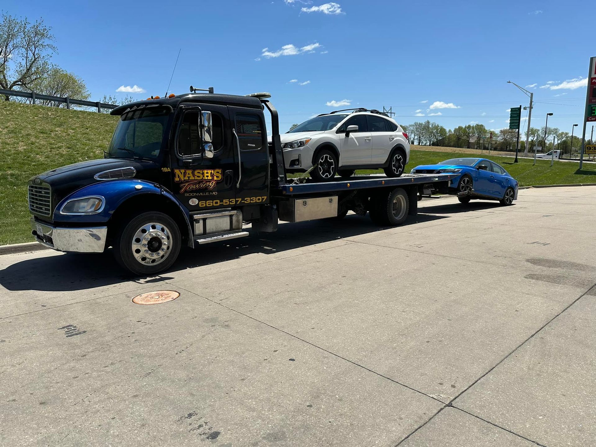 Tow truck hauling a white SUV and blue sports car on a sunny day.